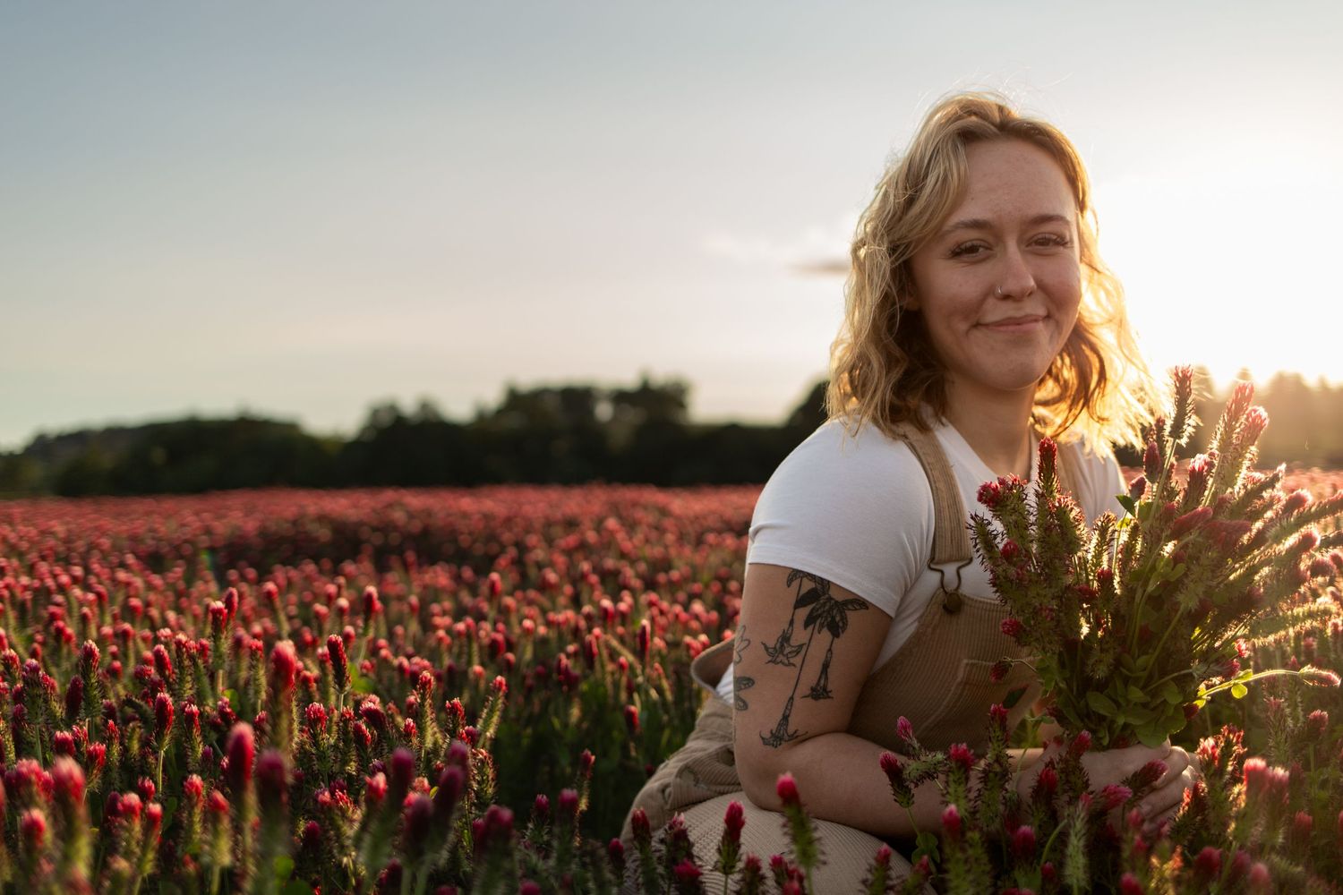Person holding wildflowers in field of red tulips during golden hour.