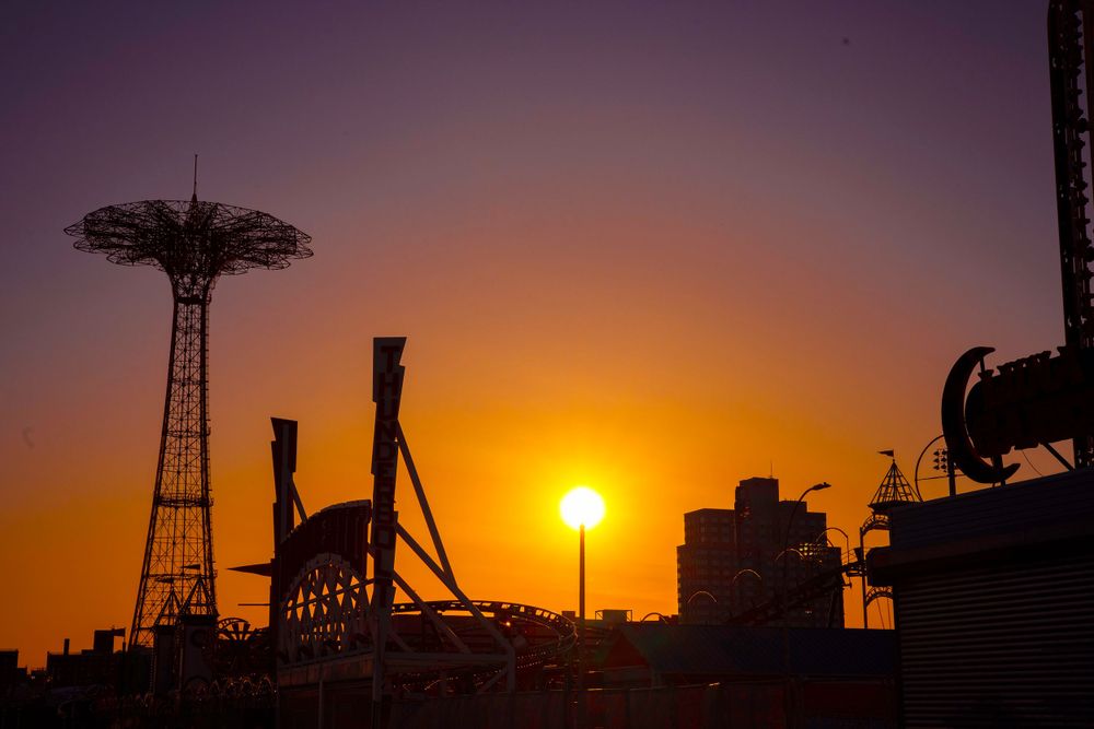 Iconic Coney Island Parachute Jump tower silhouetted against vibrant orange sunset sky in Brooklyn.