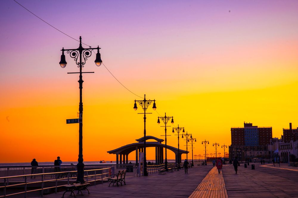 Boardwalk lampposts line up against colorful sunset sky at Coney Island.