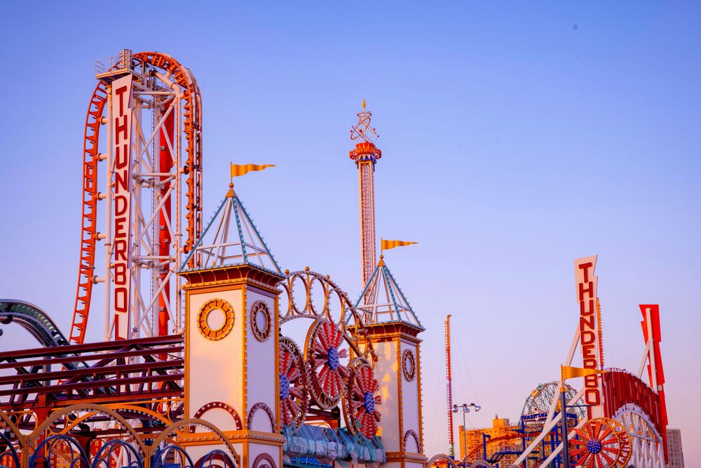 Colorful amusement park rides and attractions lit up against a twilight sky.