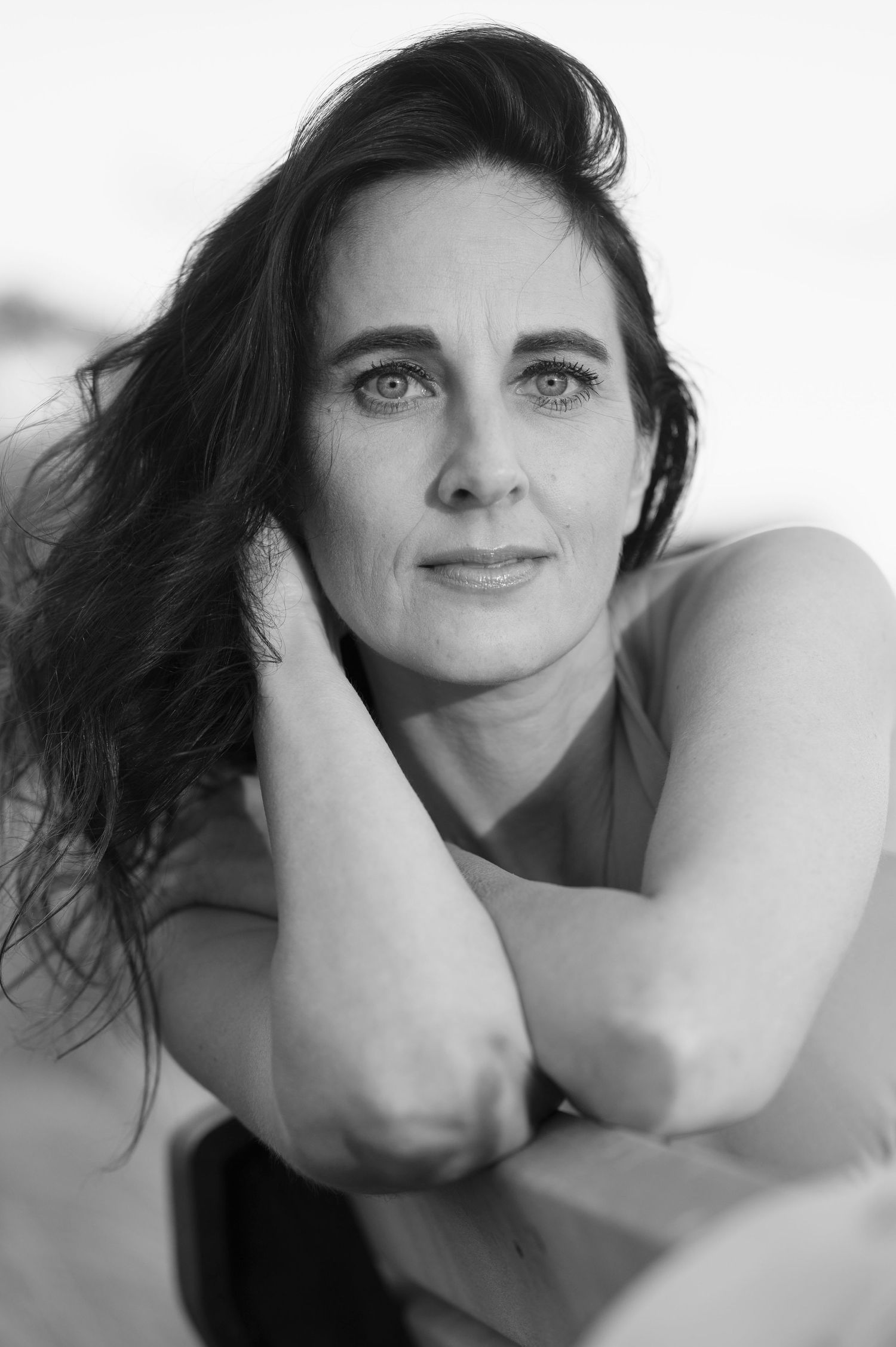 Black and white portrait of dark-haired woman with blue eyes resting chin on hands.
