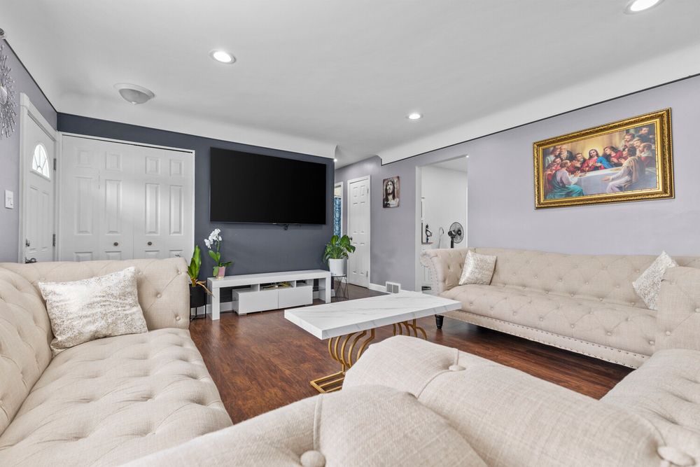 Elegant living room with cream tufted sectional sofas, hardwood floors, TV, and recessed lighting.