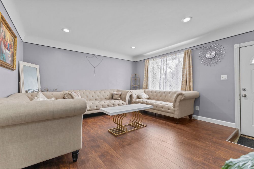 Spacious living room with beige tufted sofas, hardwood floors, and gray walls with crown molding.