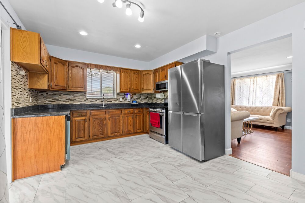 Kitchen with brown wood cabinets, stainless steel refrigerator, and mosaic tile backsplash.