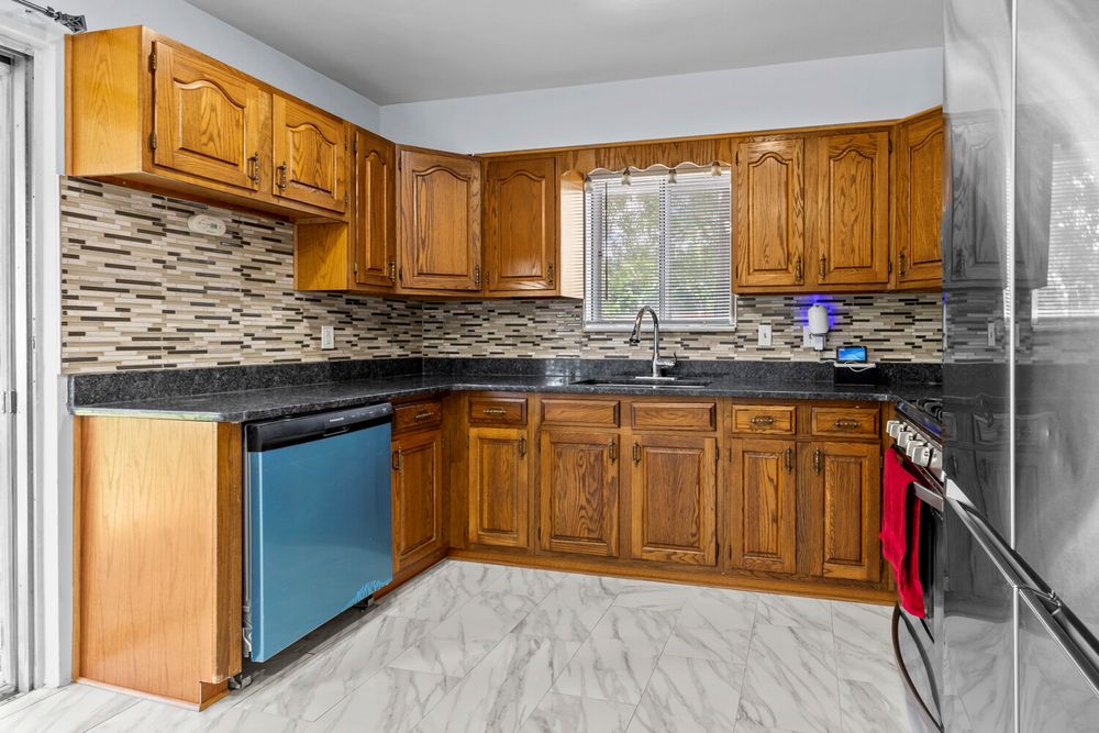 Kitchen featuring brown cabinetry, granite countertops, mosaic backsplash, and black dishwasher.