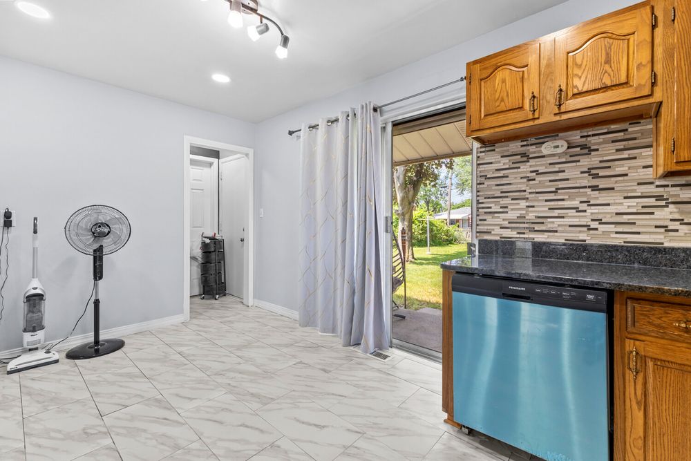 Kitchen area with wood cabinets, tile backsplash, blue dishwasher, and sliding glass door.