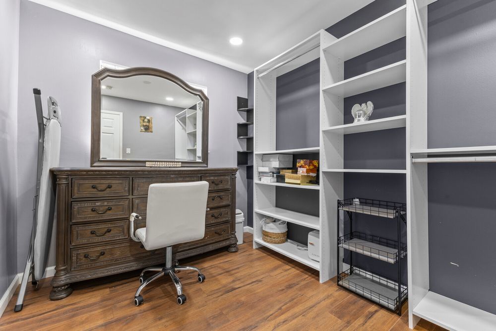 Walk-in closet with white built-in shelving, dark wood dresser, and hardwood floors.