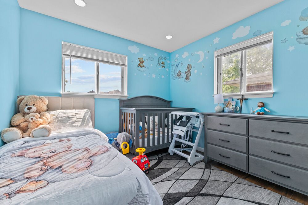 Blue childrens bedroom with crib, gray dresser, and playful wall decals.