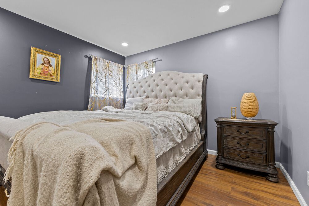 Cozy bedroom with tufted headboard, dark wood nightstand, and gray walls.