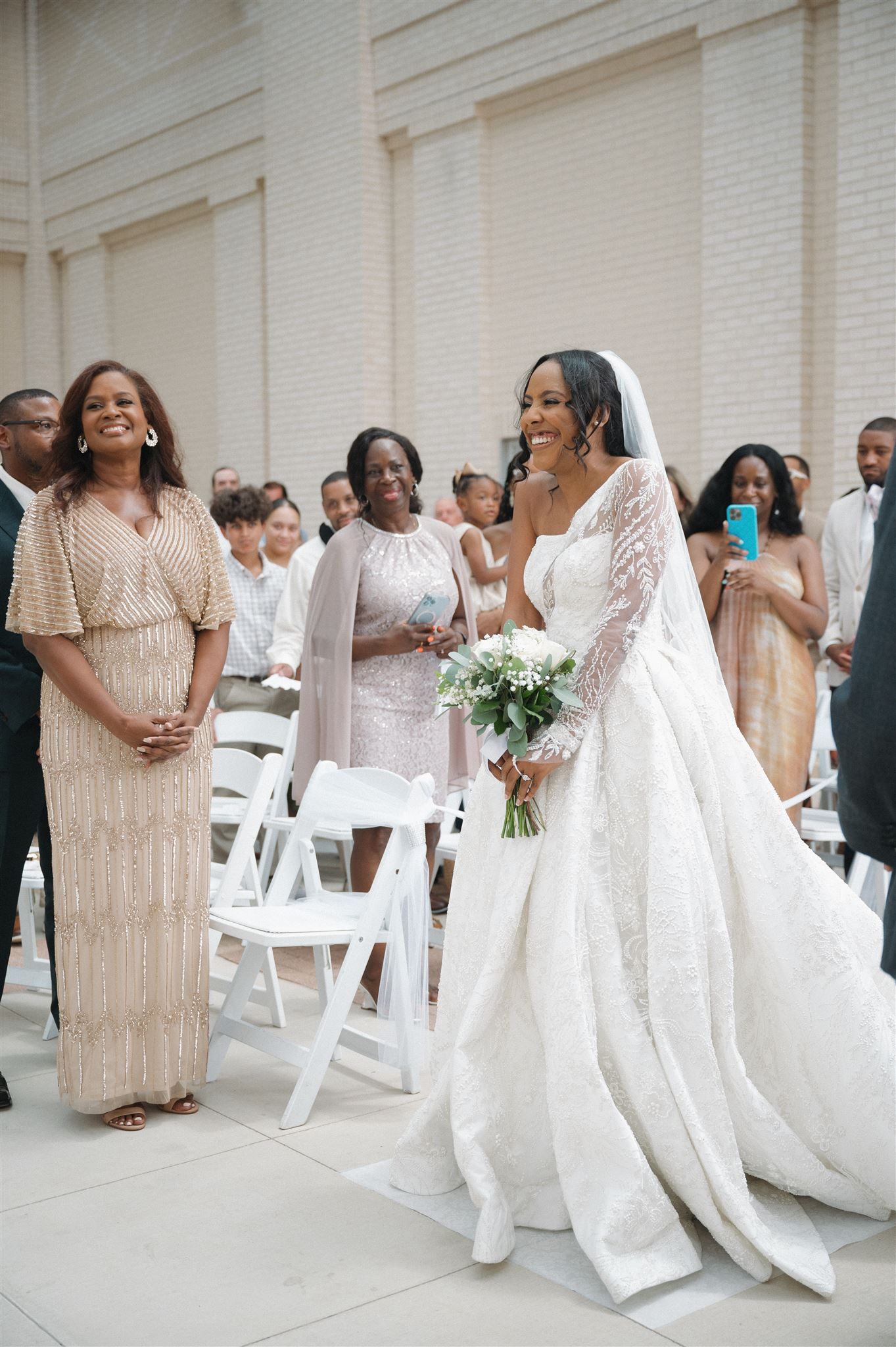 An elegant wedding ceremony with guests seated in white chairs and a bride wearing a stunning long-sleeved lace gown.