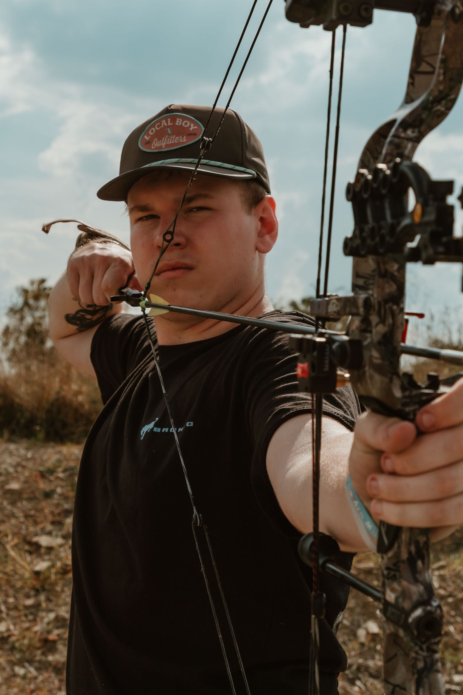 Close-up view of an archer drawing back a compound bow while practicing target shooting outdoors.
