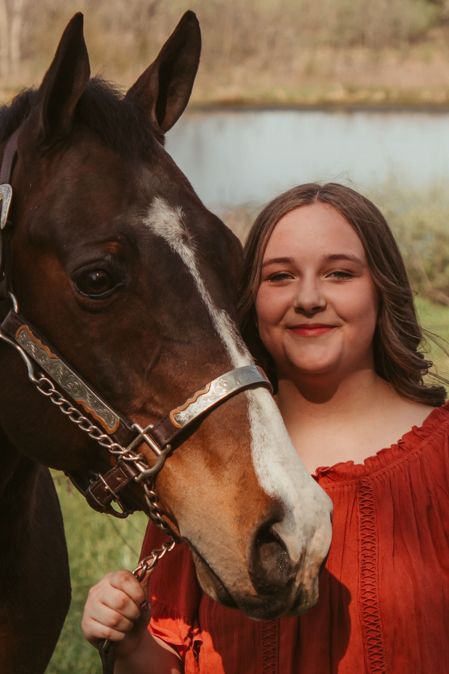 A brown and white horse nuzzles close to someone wearing a bright red sweater in an outdoor setting.