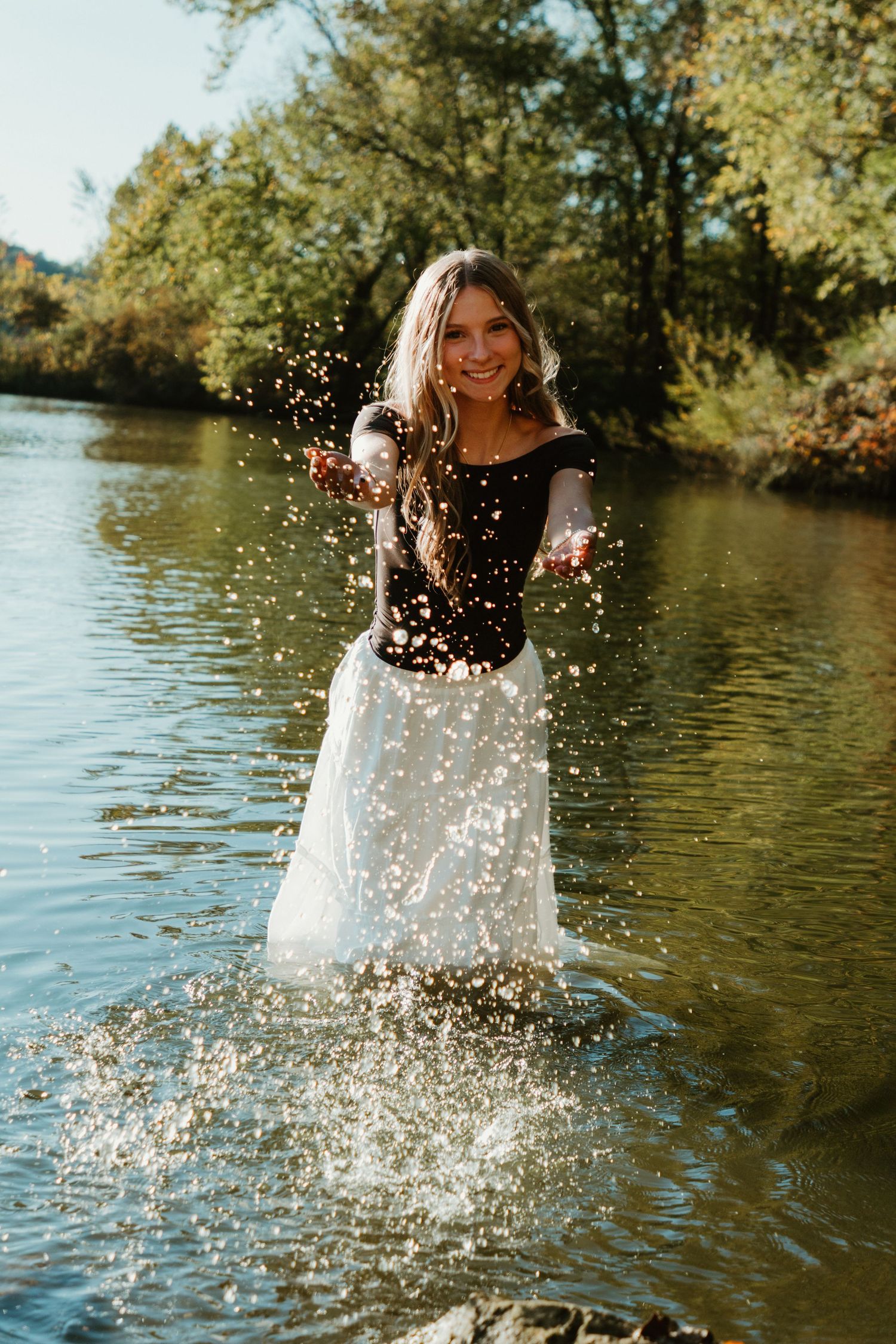 Joyful splashing in a lake creates sparkling water droplets while wearing a black and white dress.