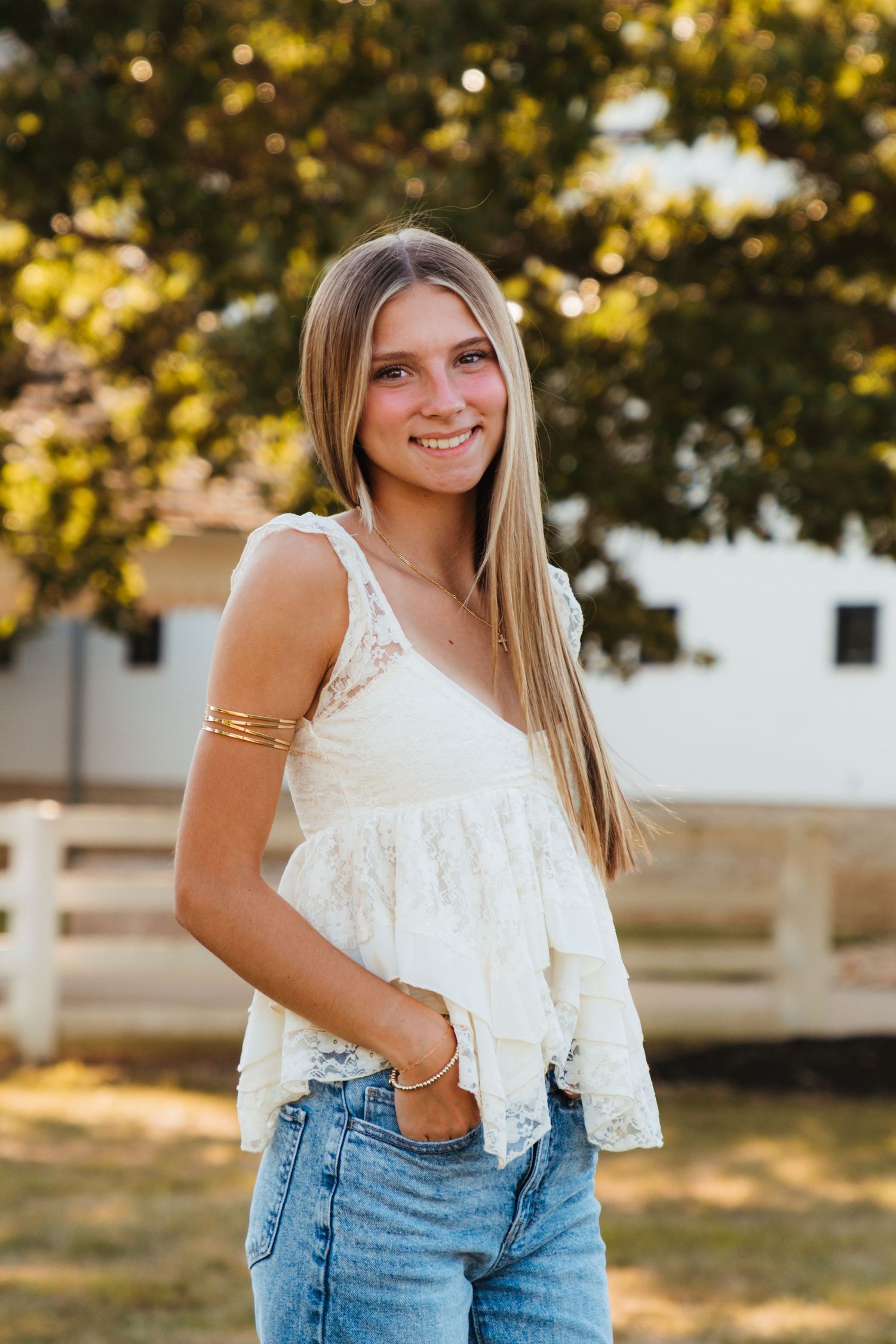 A person wearing a white lace top and blue jeans poses outdoors in natural lighting.