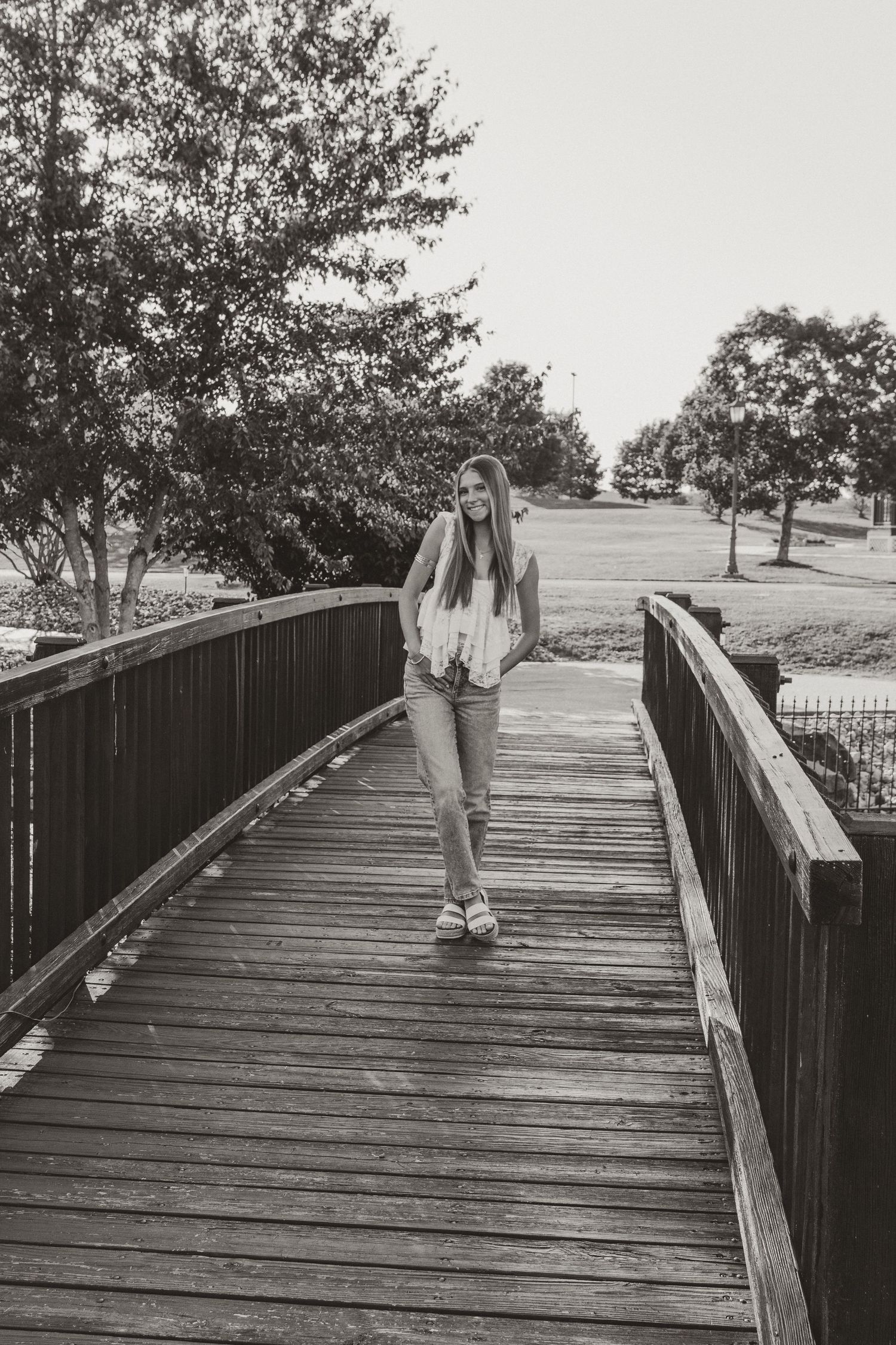 A sequence of black and white photos showing someone walking across a wooden bridge or boardwalk in a park setting.