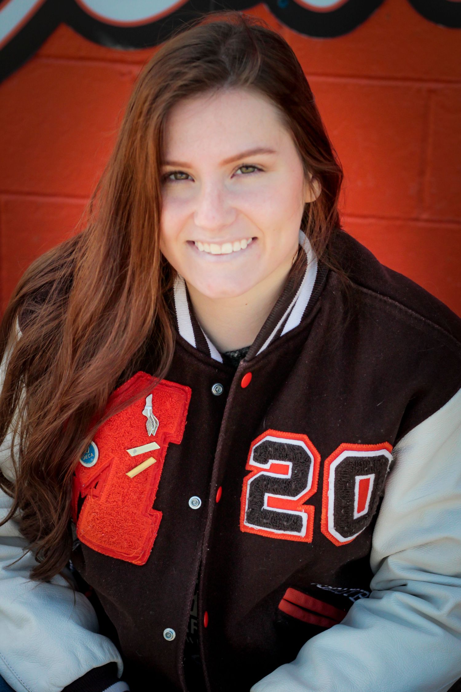 Student wearing a varsity letterman jacket with number 20 and red accents against an orange background.