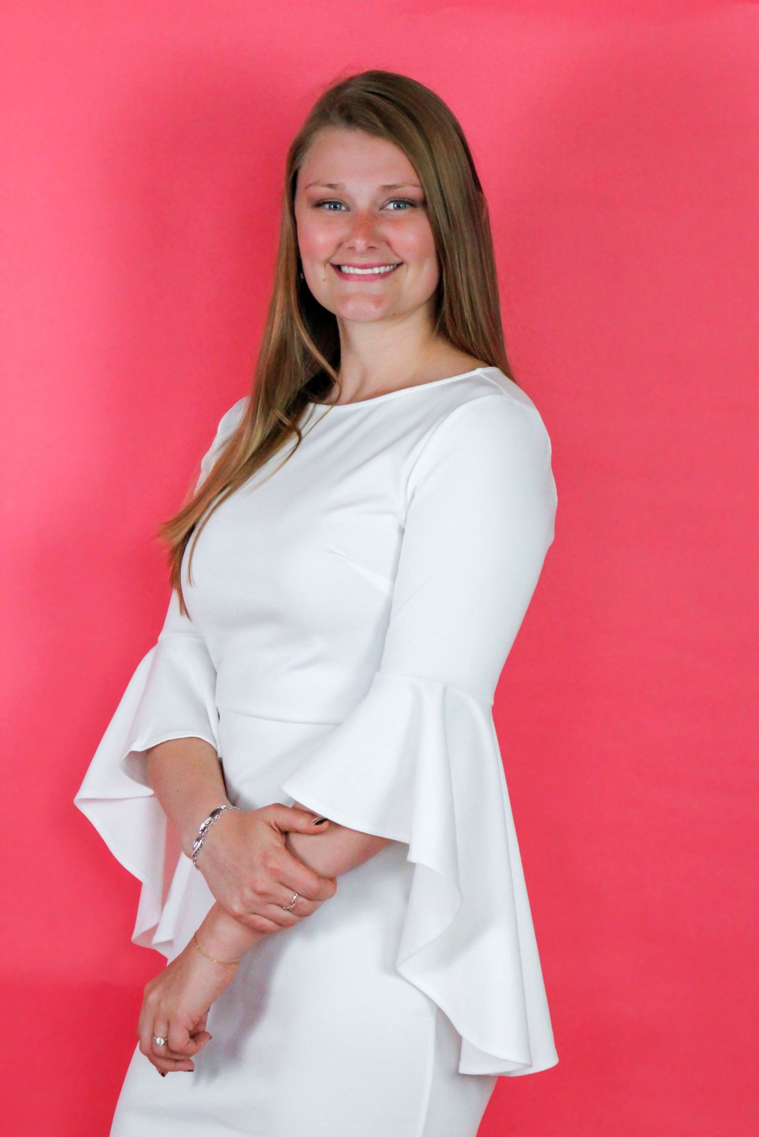 Portrait of someone in elegant white bell-sleeve dress against pink backdrop.