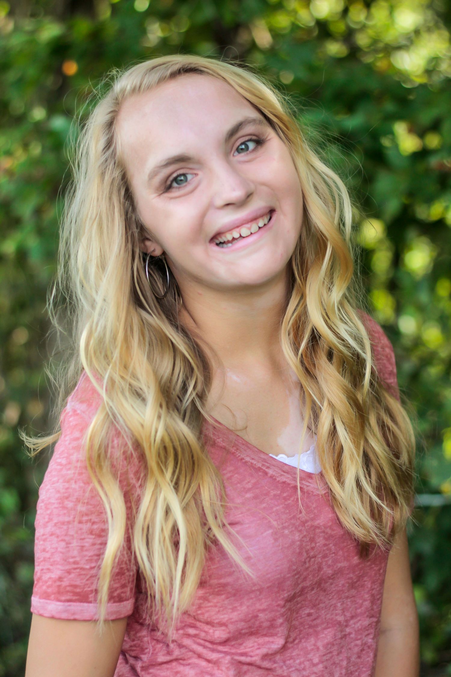 A casual portrait outdoors wearing a pink top against blurred greenery.