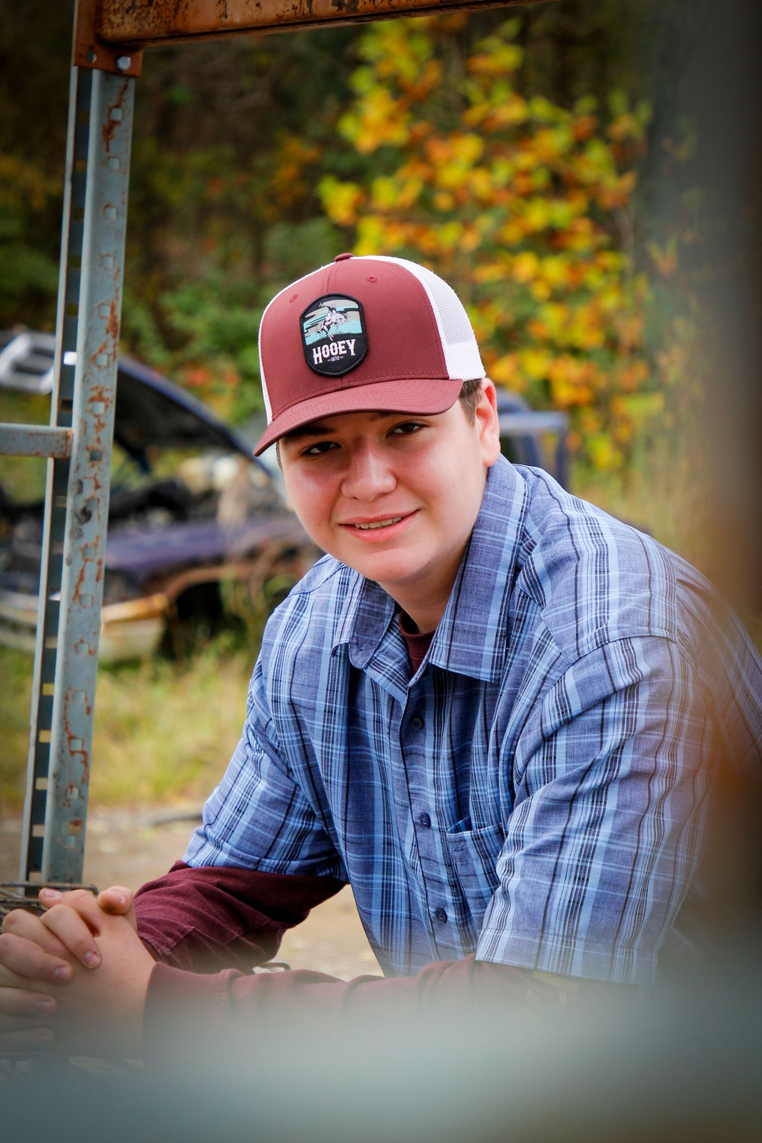 Casual outdoor portrait in plaid shirt and baseball cap against fall foliage.