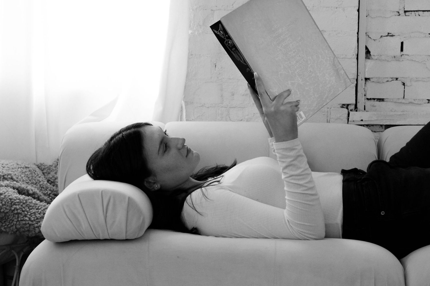Black and white photo of person reading while lying down.