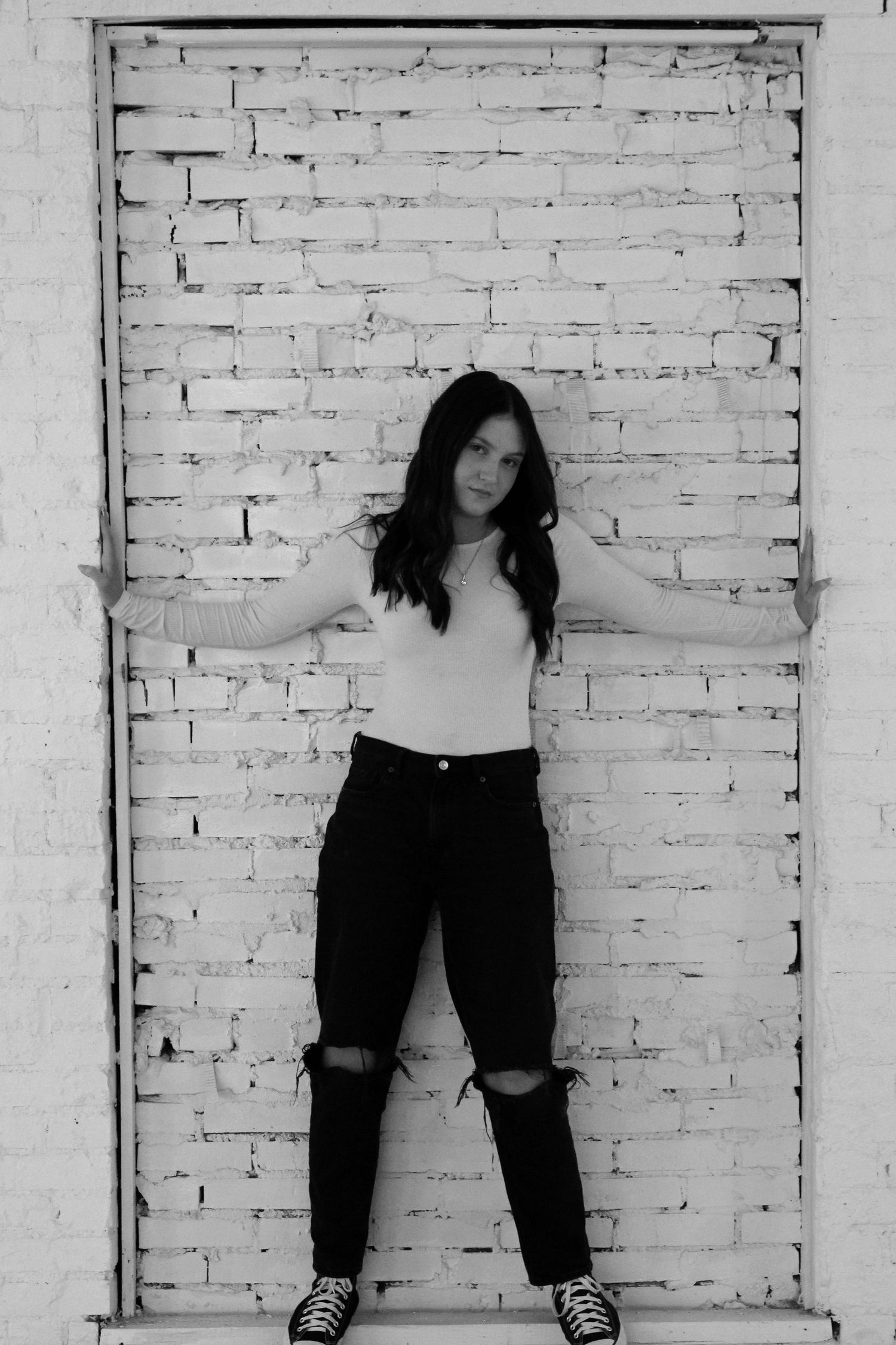 Black and white portrait against white brick wall wearing casual attire.
