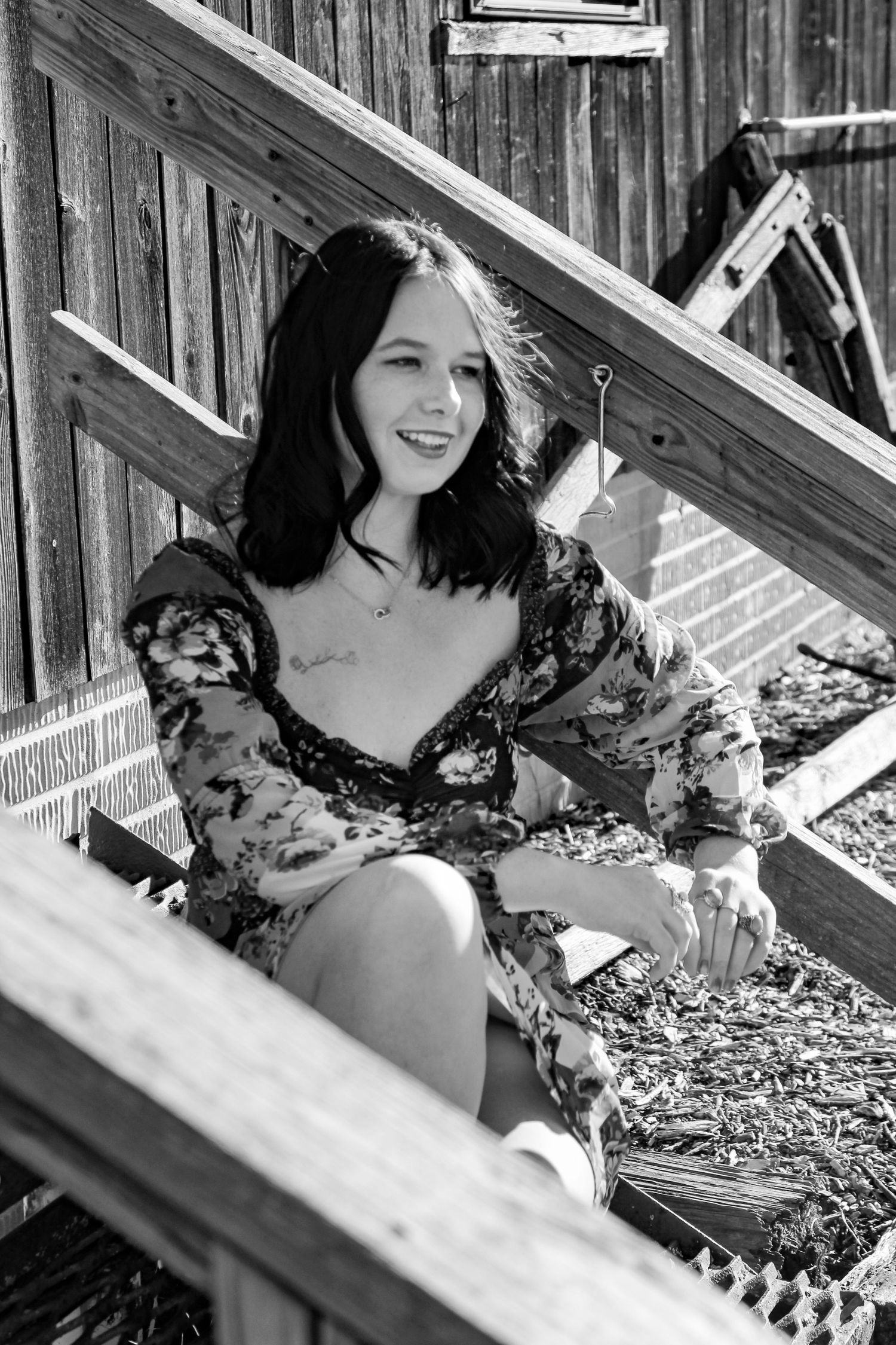 A black and white portrait of someone in a floral dress sitting on wooden steps.