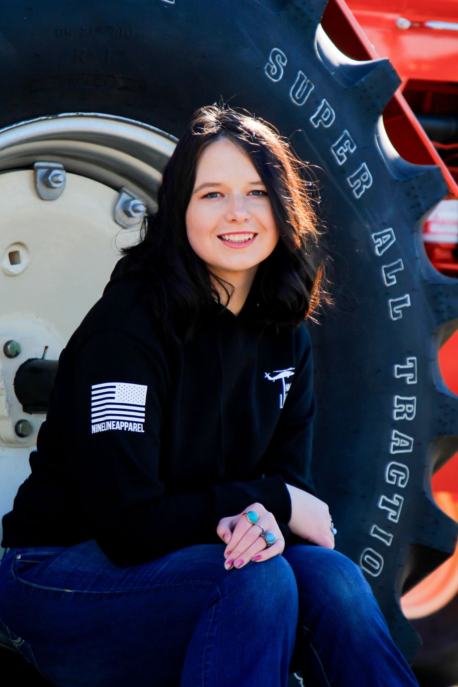 A casual portrait next to a large tractor tire wearing a black hoodie with American flag patch.