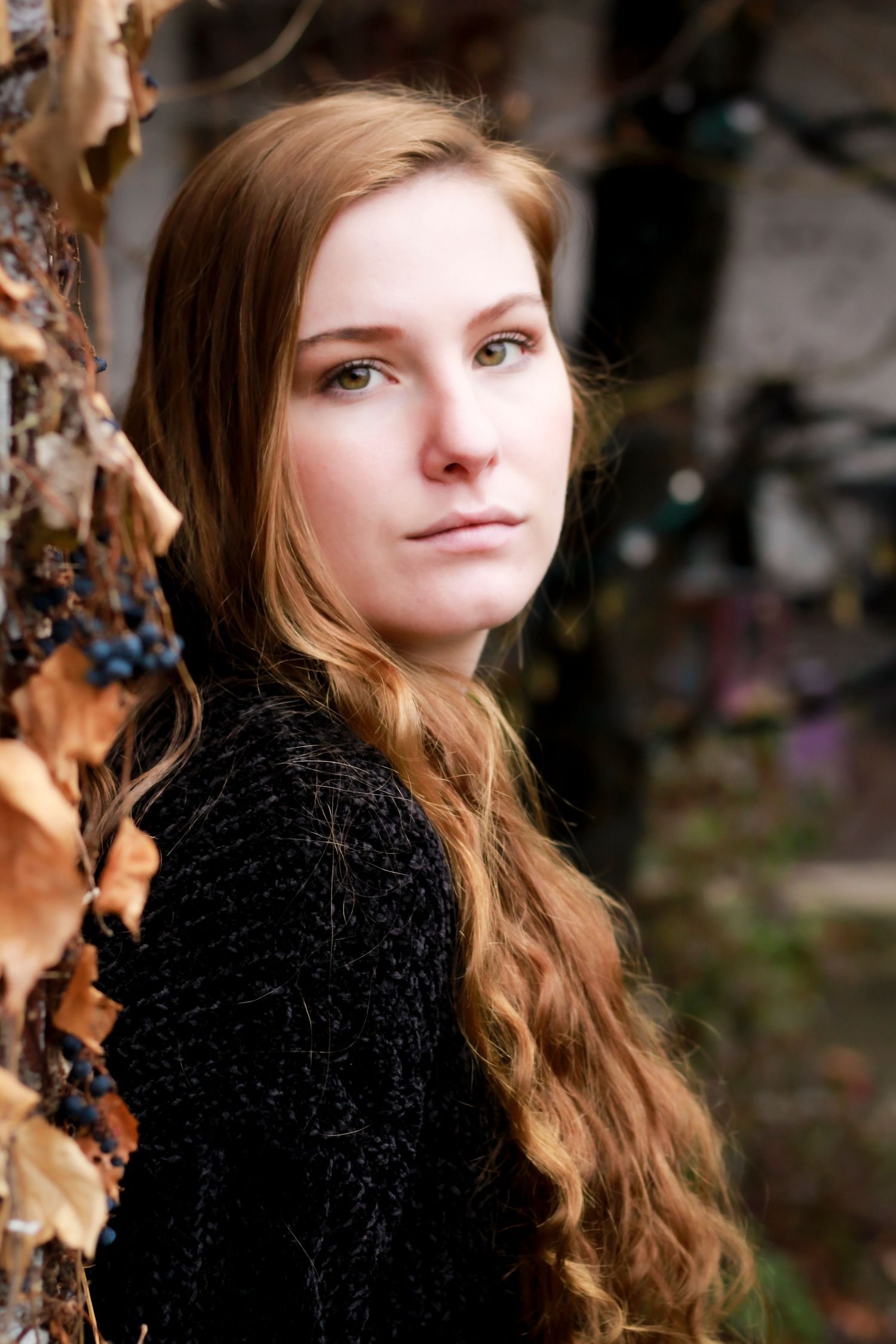 Artistic portrait against autumn foliage background wearing black velvet top.