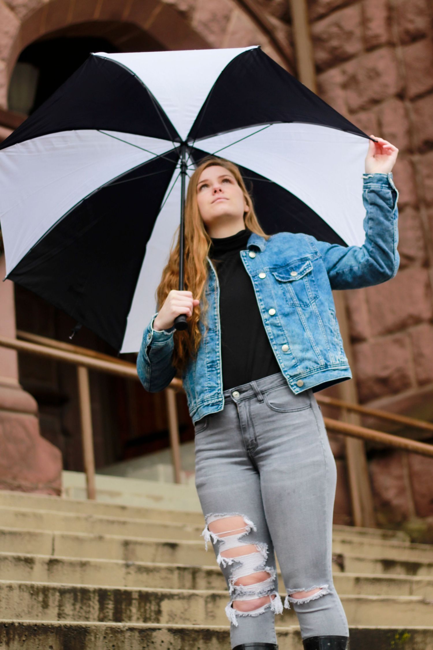 Stylish portrait with black and white umbrella on stone steps wearing distressed jeans and denim jacket.