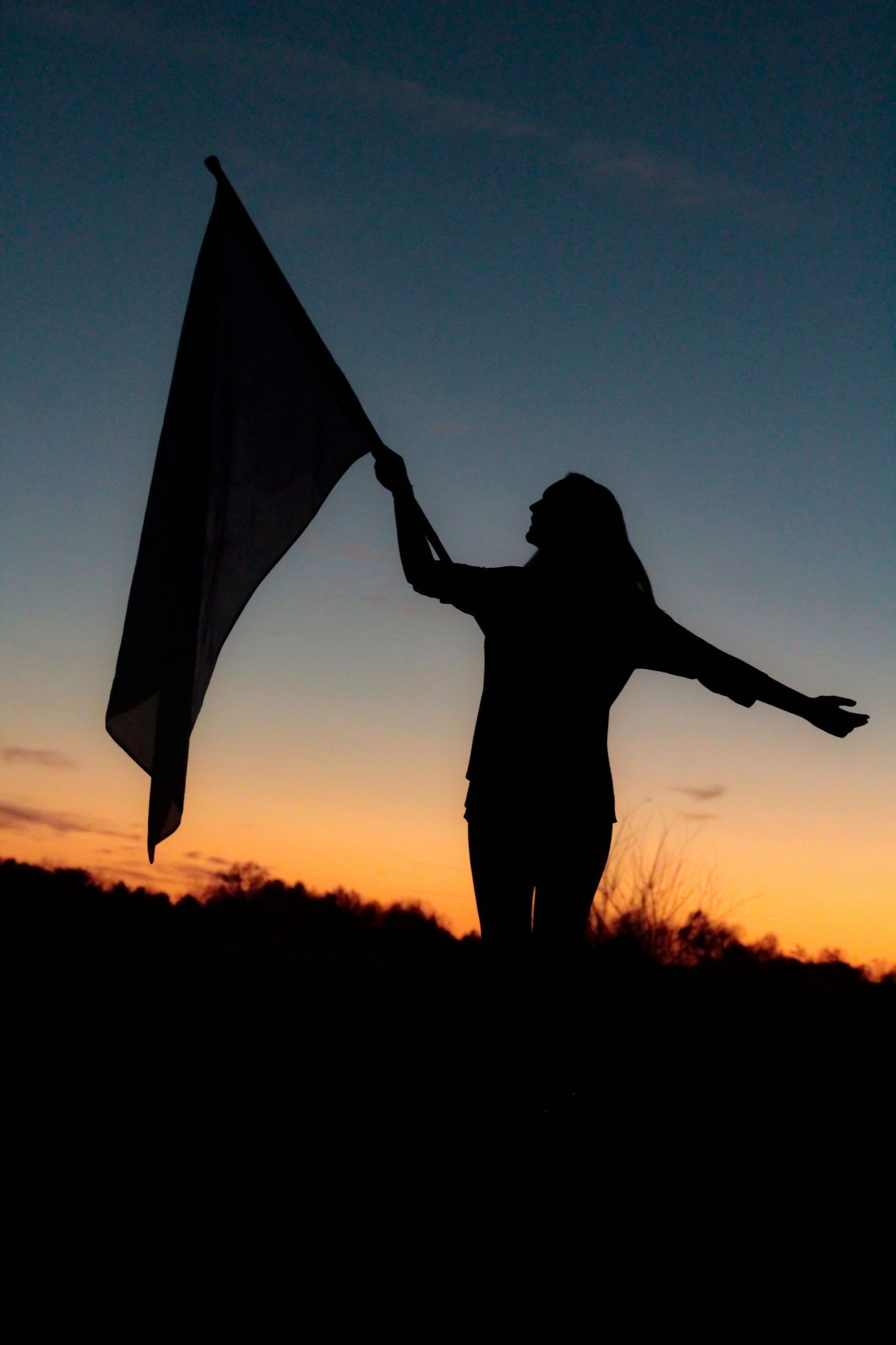 A silhouette holds a flag against a dramatic sunset sky.