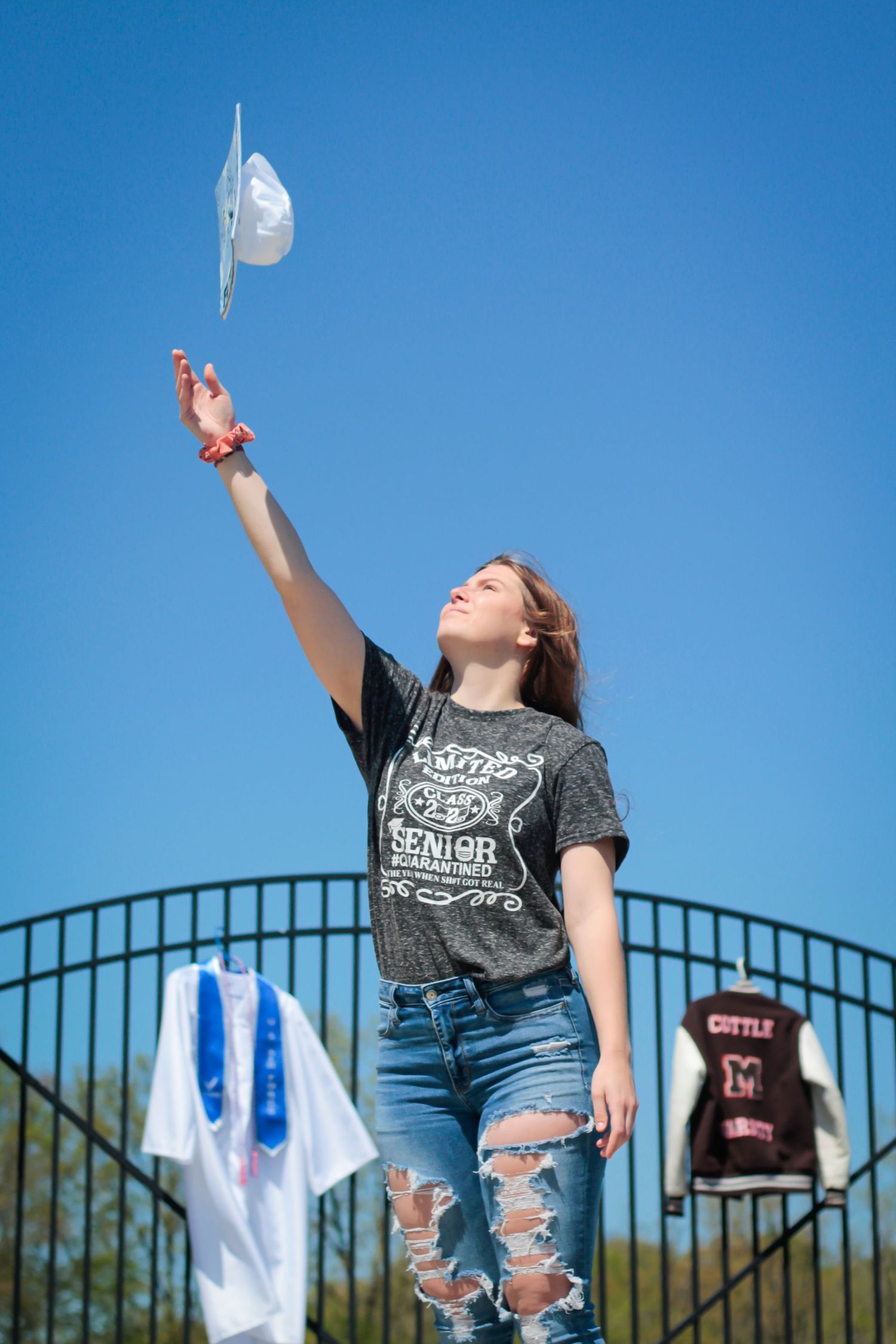 Person in ripped jeans and graphic t-shirt reaching up towards the sky with graduation cap.