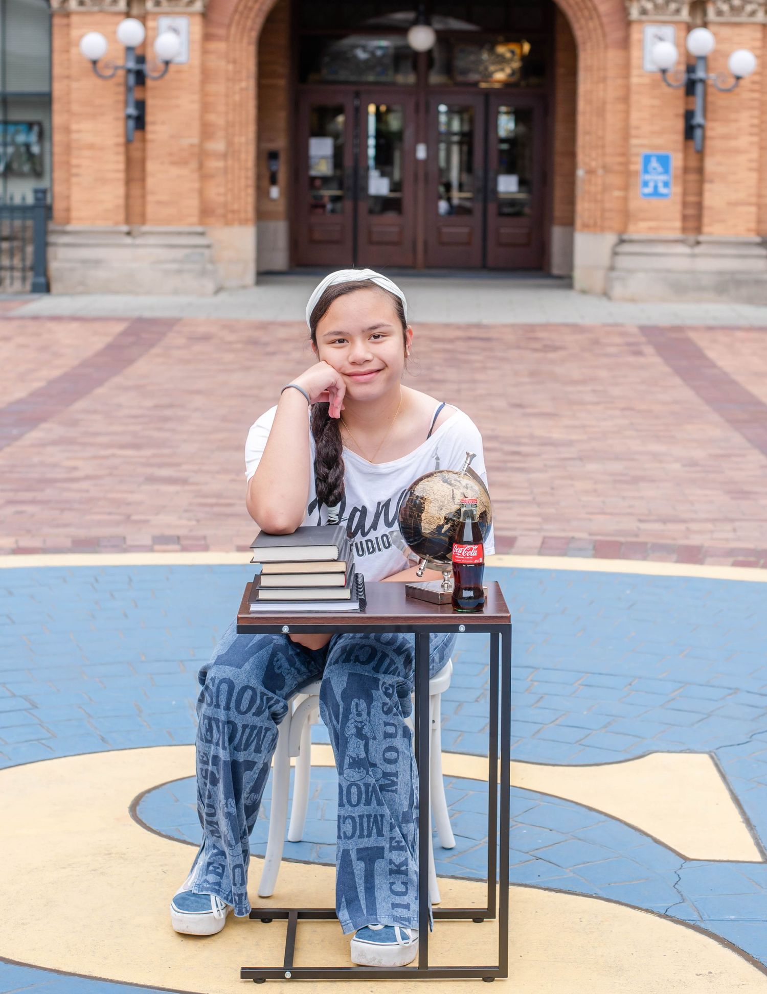 Student studies at outdoor table against backdrop of ornate brick building and blue pavement.