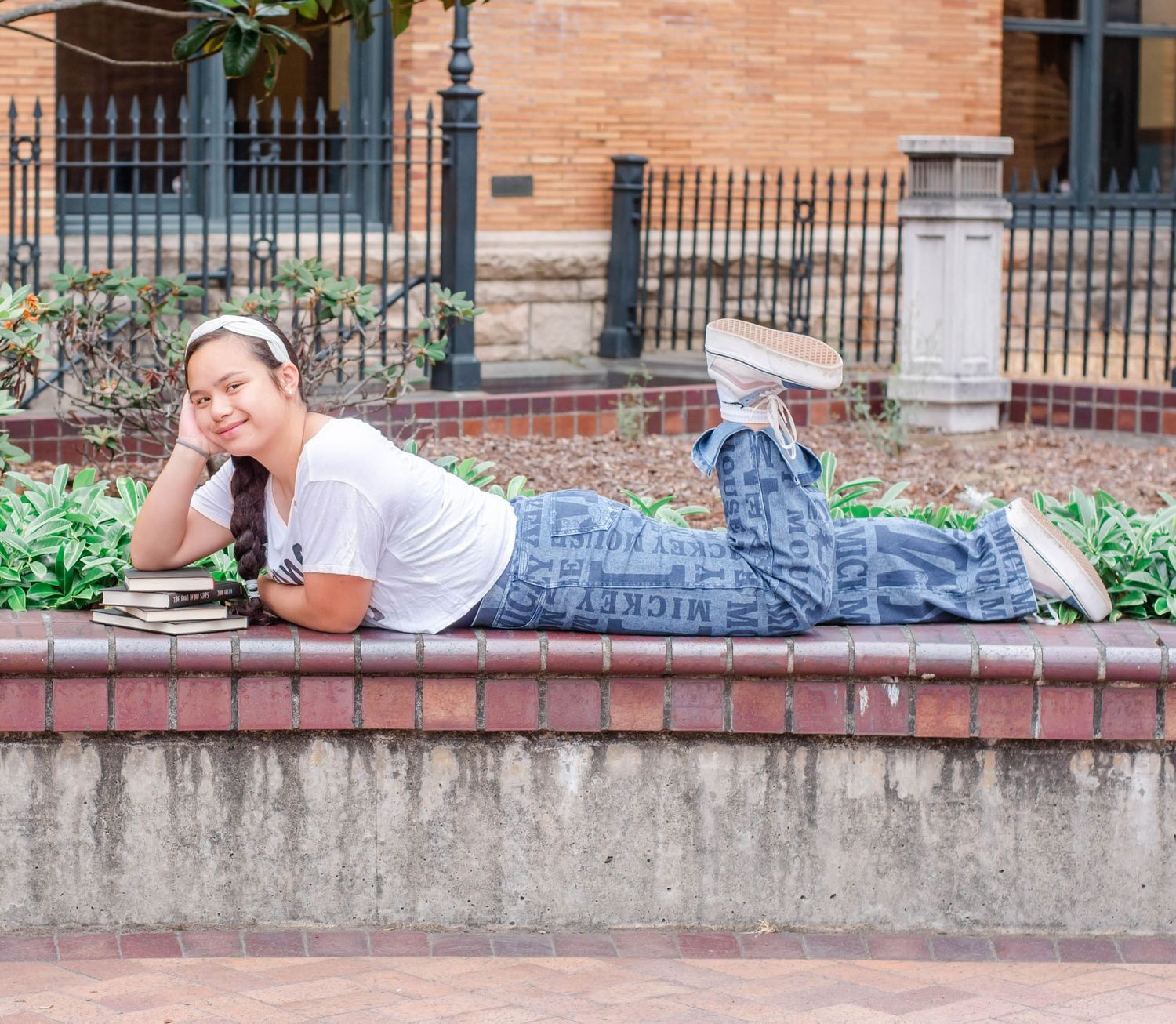 Student relaxes on brick ledge with books while studying outdoors.