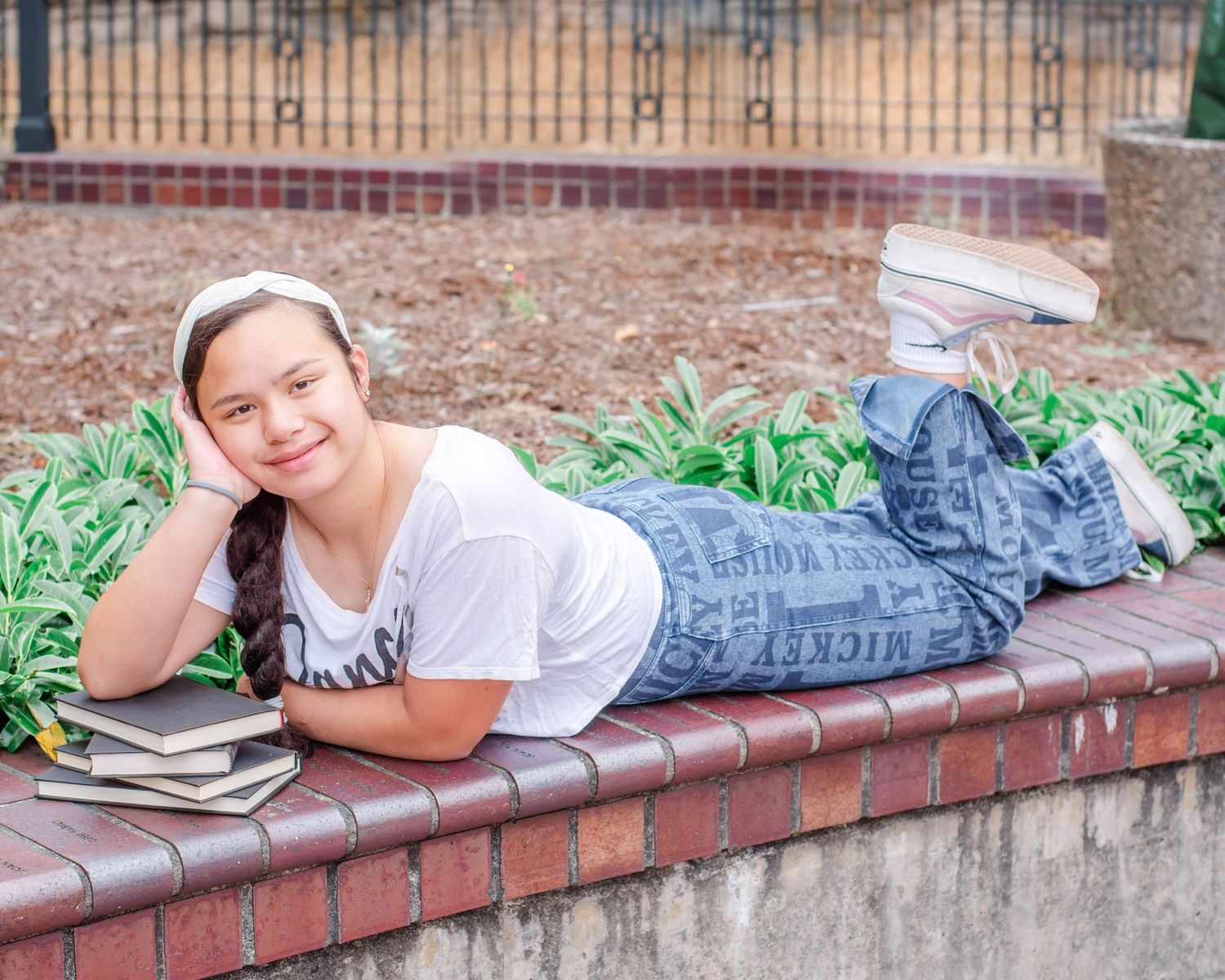 Student lies on brick wall with textbooks during outdoor study session.