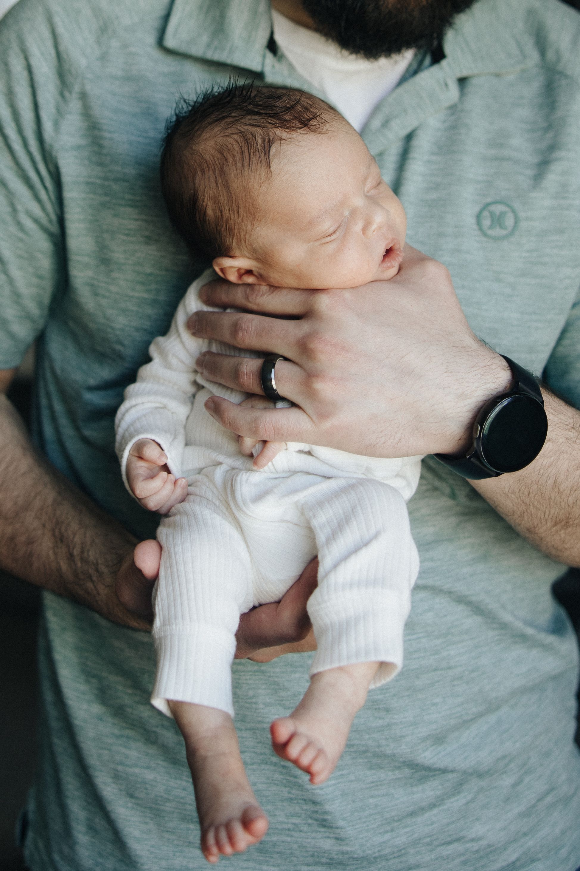 A sleeping newborn baby wearing white clothing rests peacefully in gentle supporting hands.