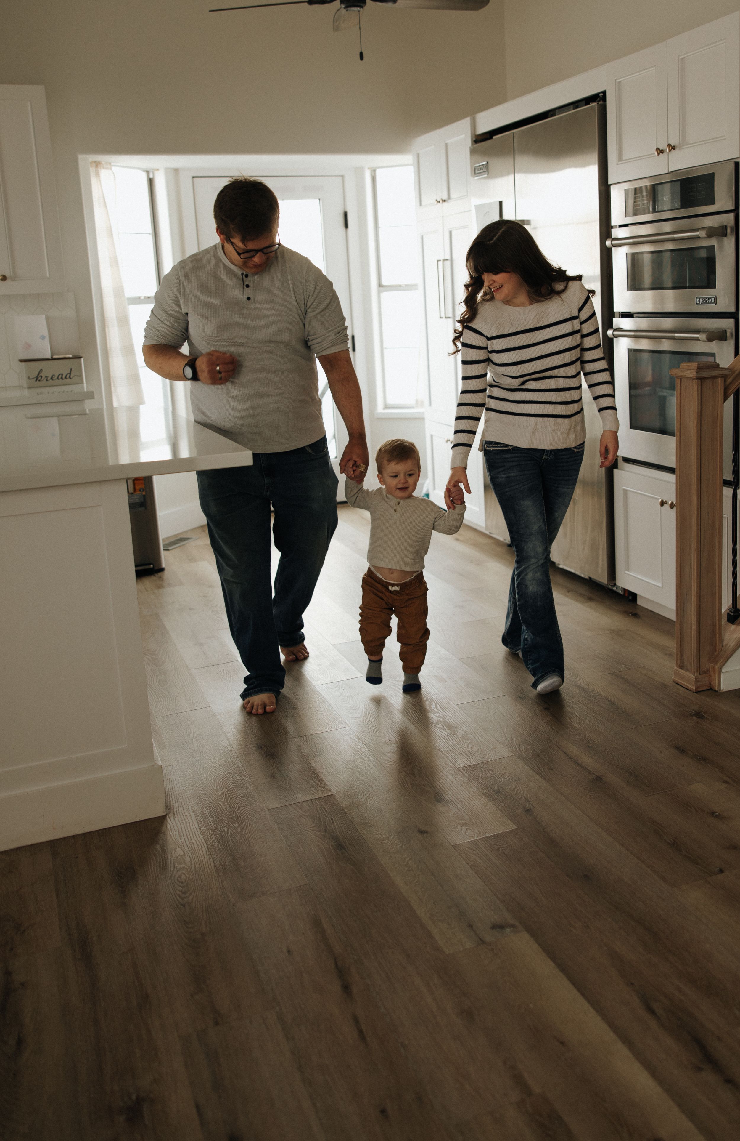 A young family walks together on hardwood floors in their modern kitchen.