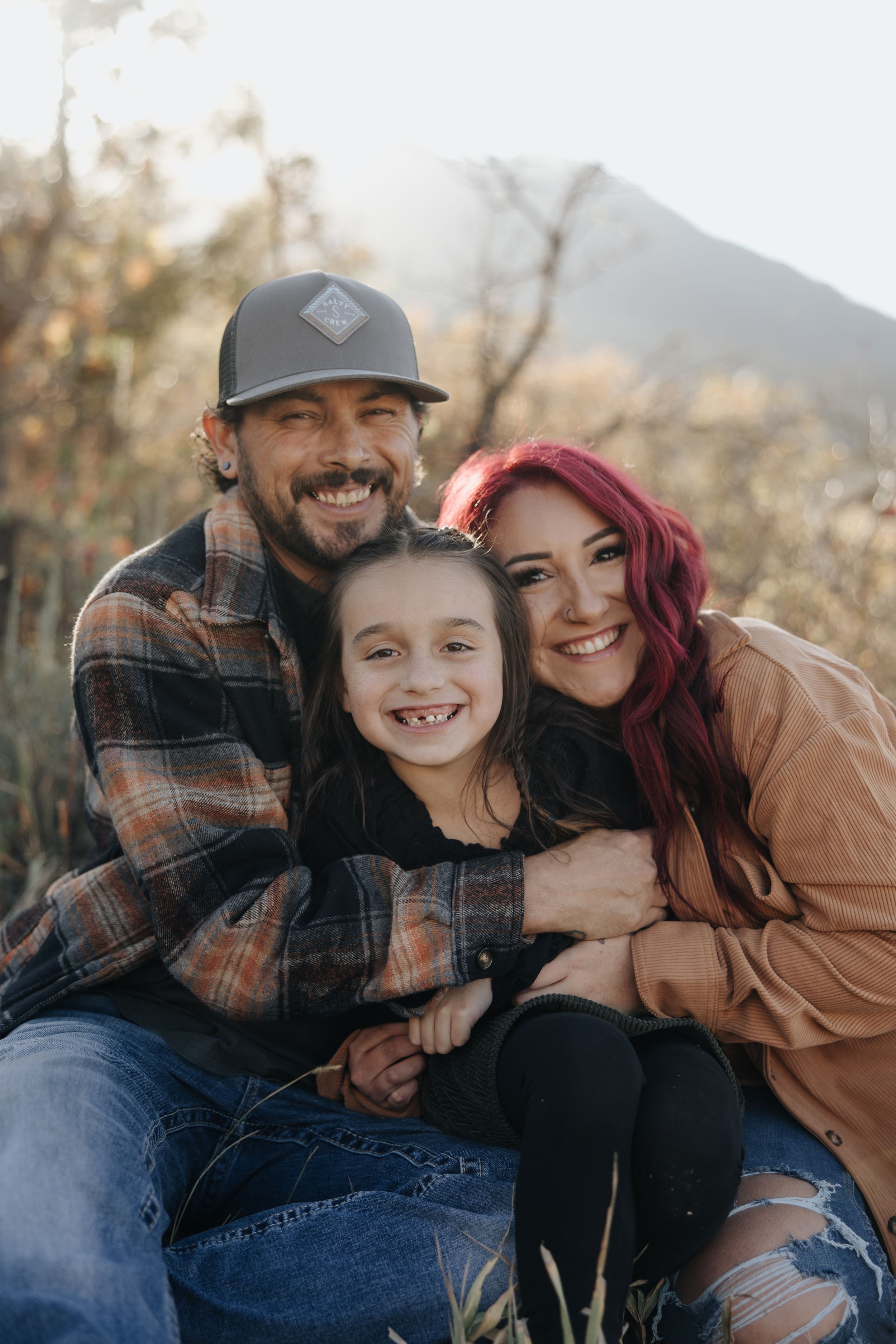 A family sits together outdoors on a fall day with a mountain visible in the background.