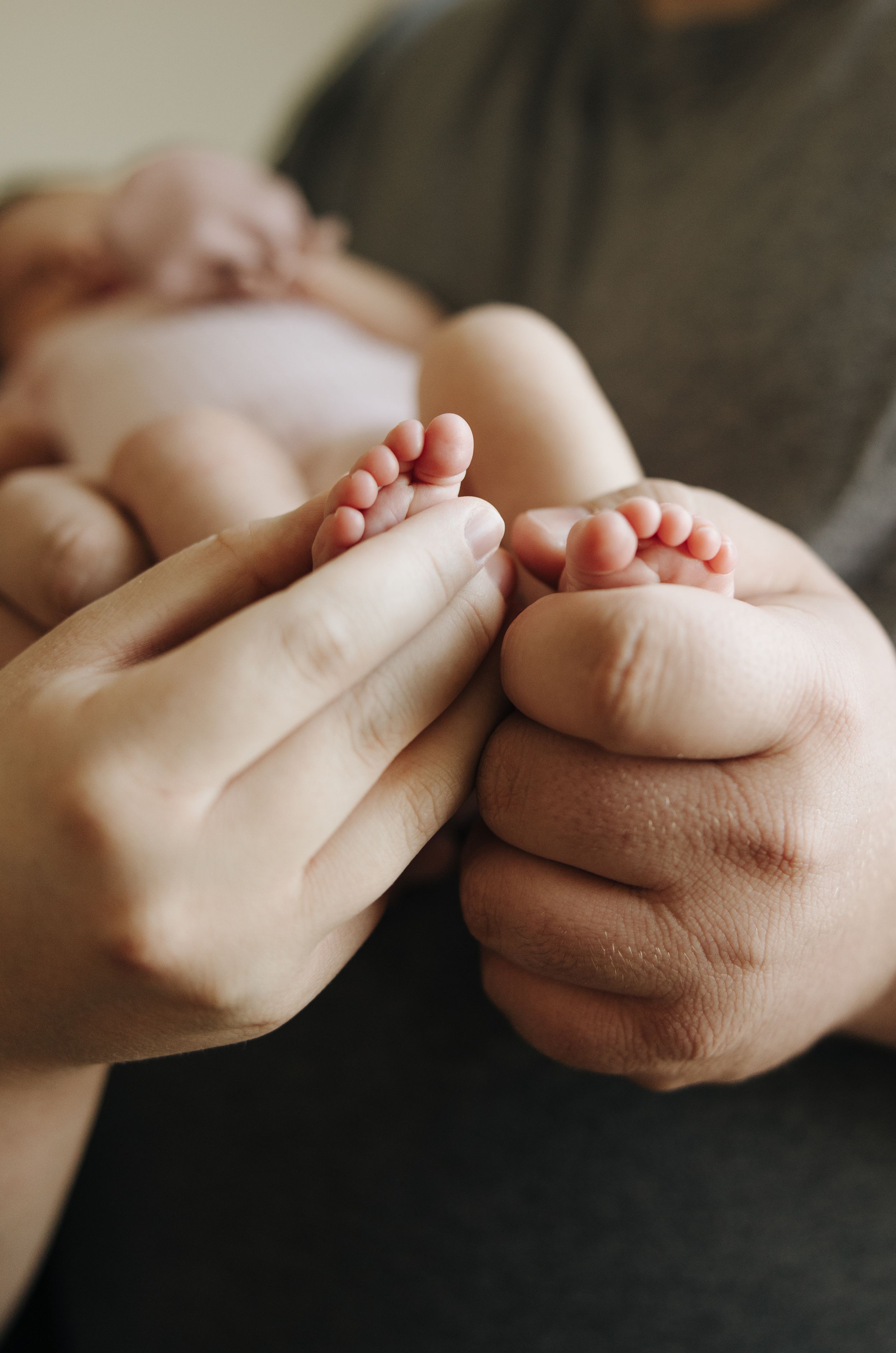 Close-up of tiny infant feet being held by adult hands against a dark background.