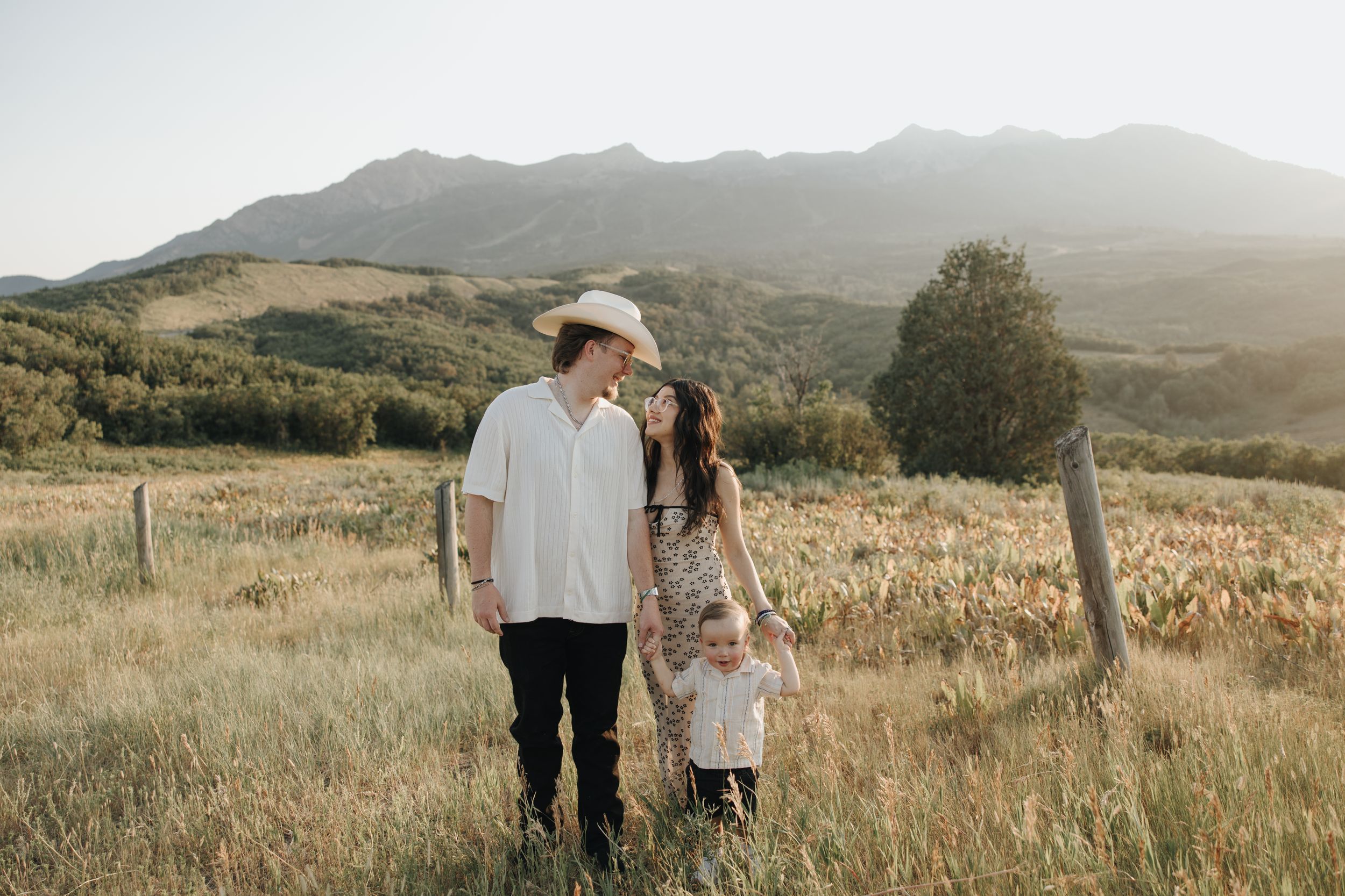 A family stands together in a golden field at sunset with mountains in the background.