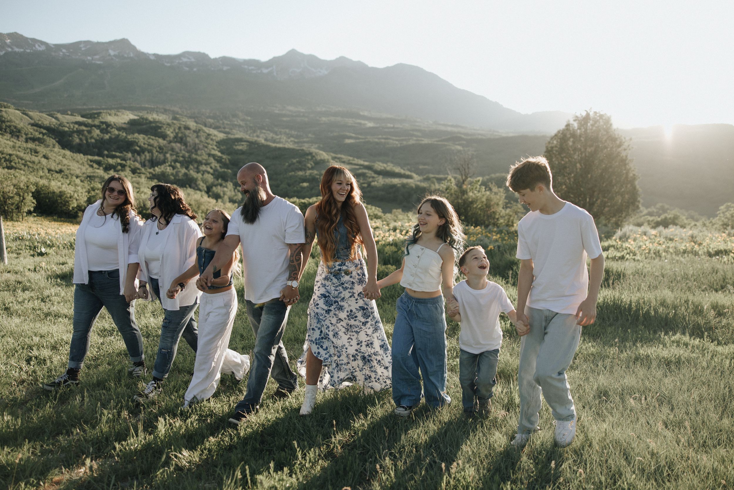 Group enjoying a sunset moment together in a scenic mountain meadow with golden light and rolling hills in background.