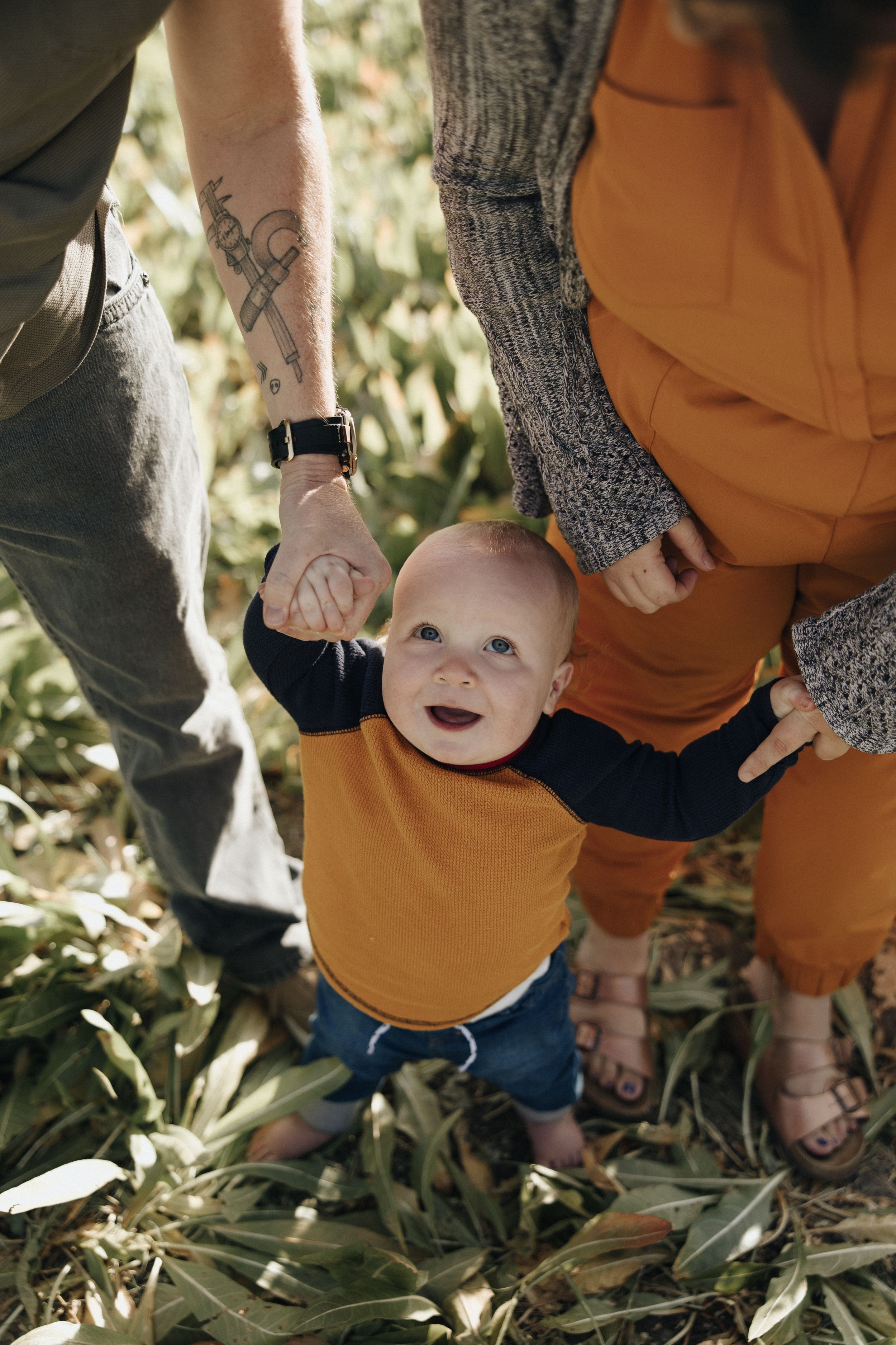 Three progressive shots showing a playful moment in nature as a baby in orange clothing laughs while being held.