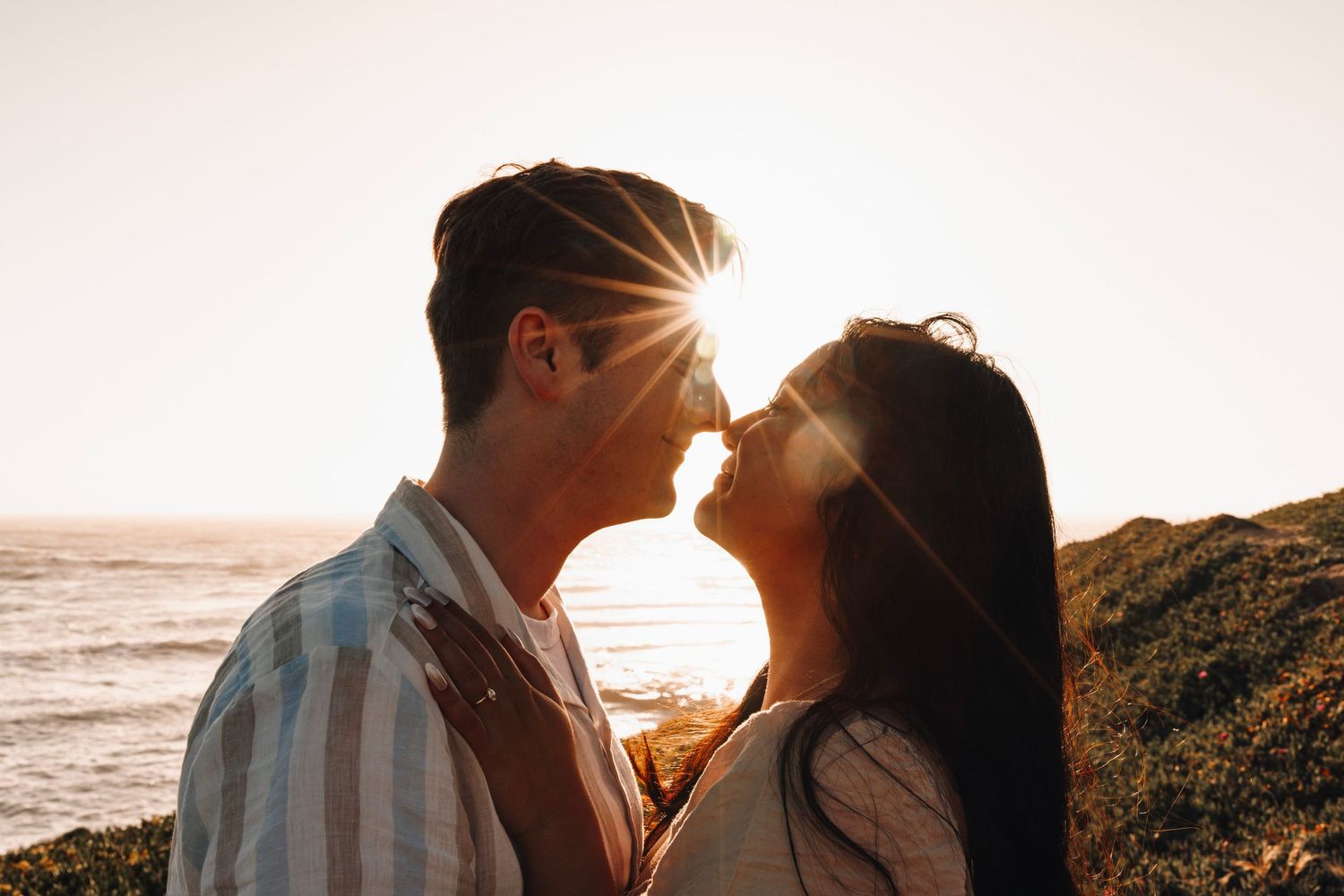 Romantic couple nearly kissing at sunset by the ocean with a beautiful lens flare effect.