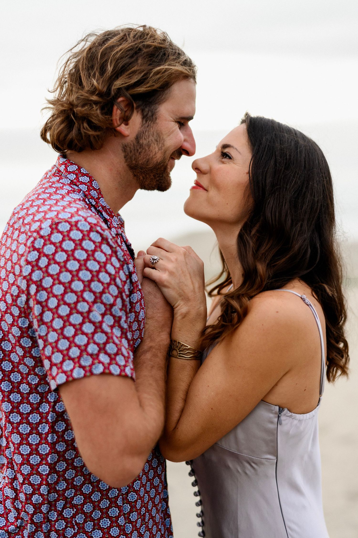 Bearded man in floral shirt and woman in sundress sharing a close moment.
