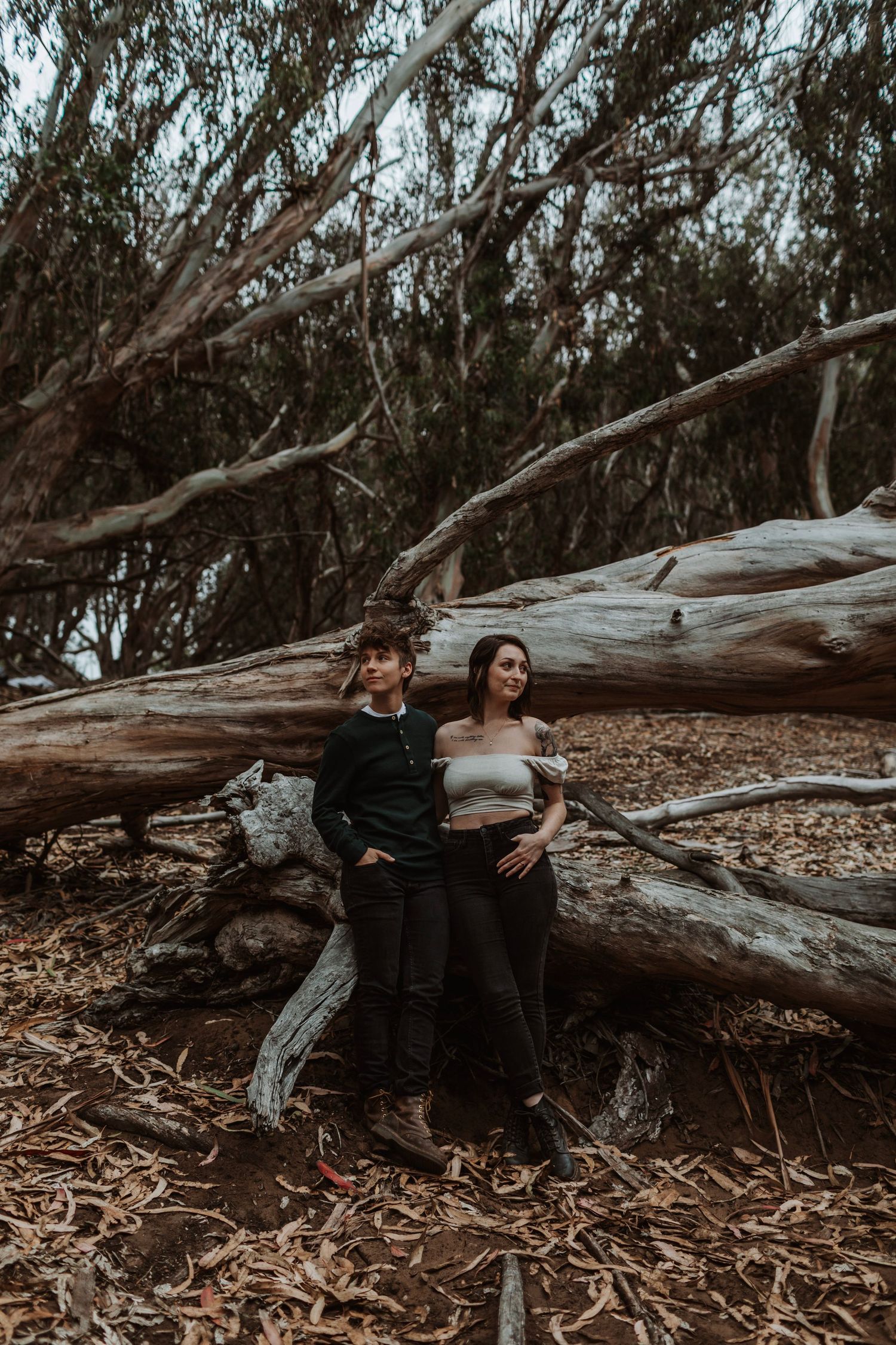 Couple leaning against fallen logs in a moody forest setting.