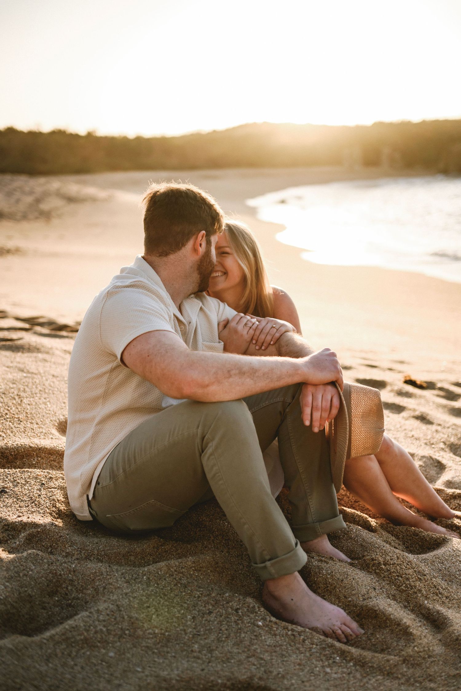 Couple sitting together on sandy beach at sunset, sharing a romantic moment.
