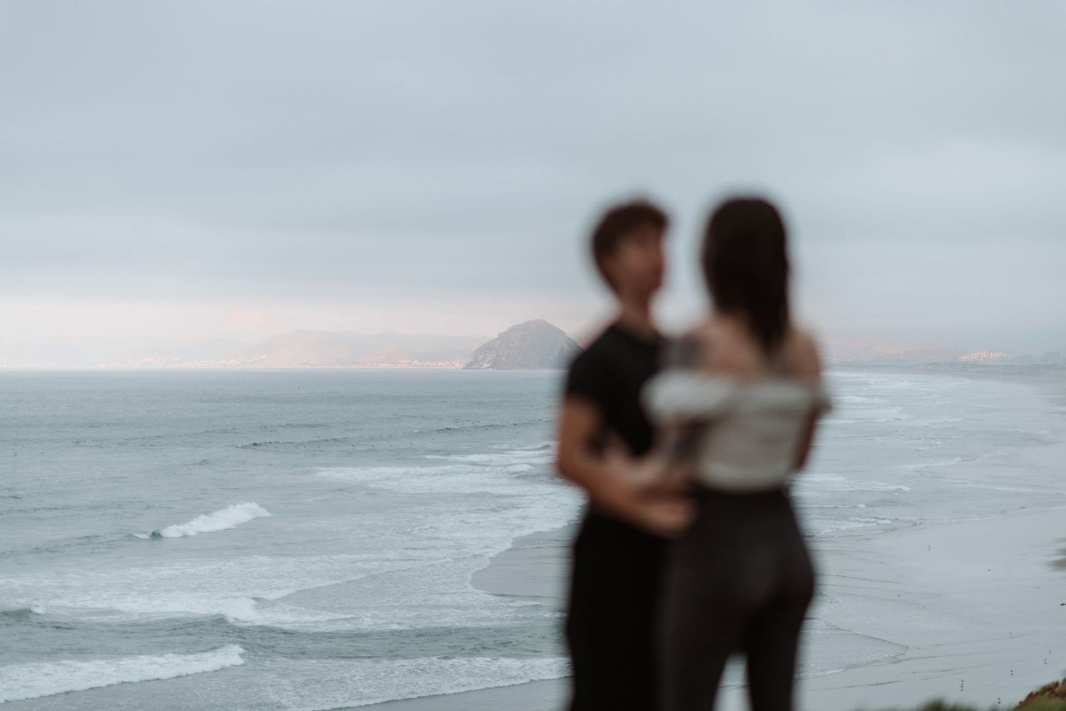 Blurred couple holding each other overlooking a scenic coastal view.