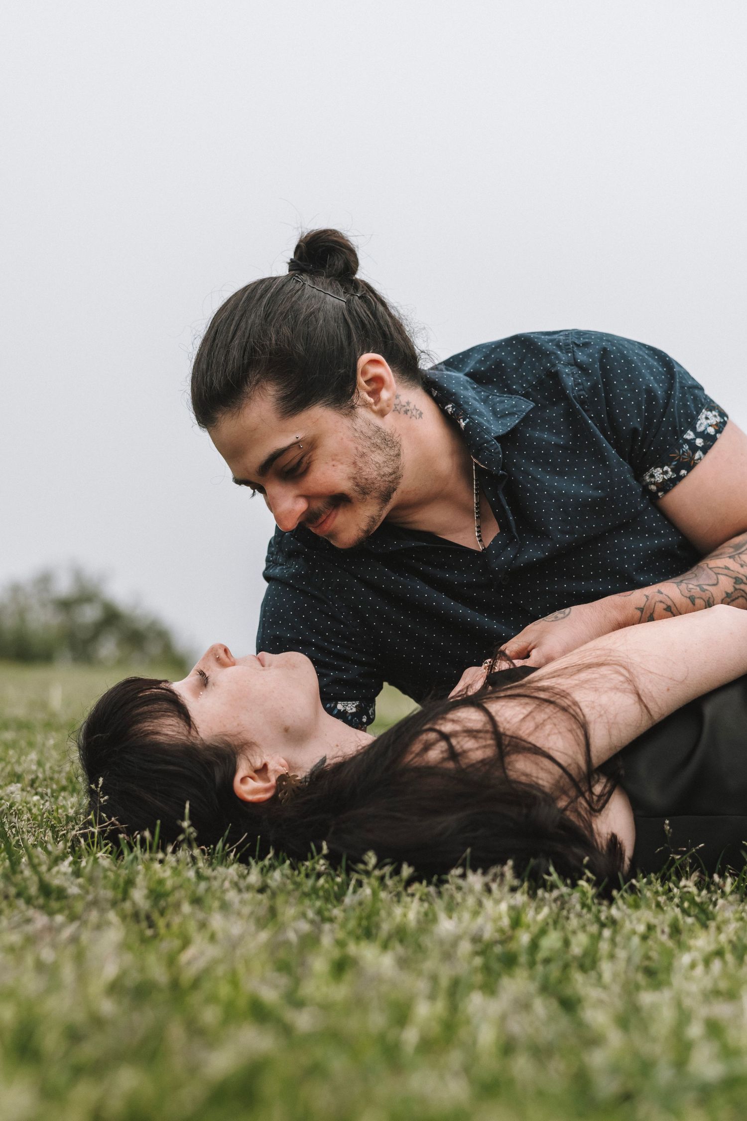A couple shares a romantic moment on green grass, with the man leaning over the woman who lies back smiling.