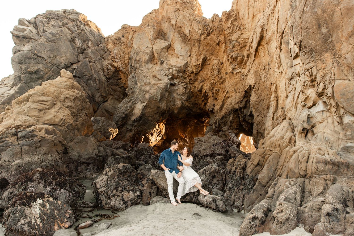 Couple embracing in a dramatic rocky sea cave on a sandy beach.