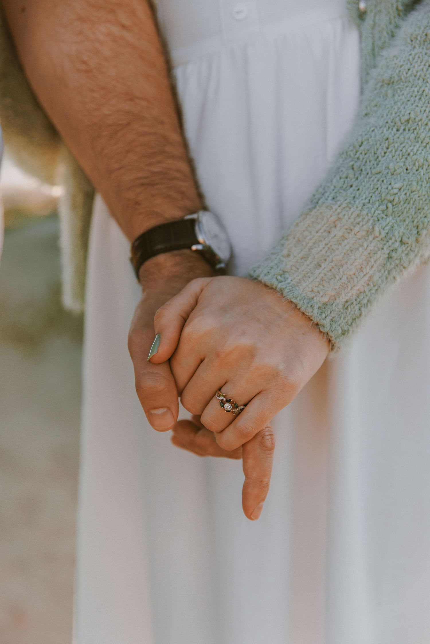 Close-up of couple holding hands with engagement ring and leather bracelet visible.