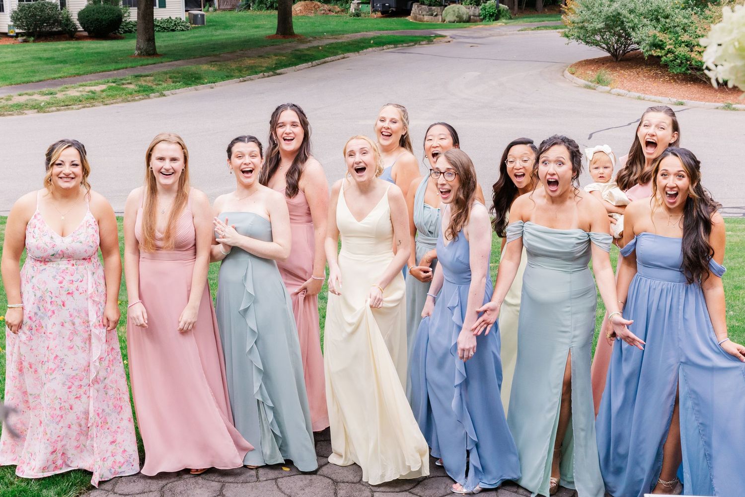 Bridal party wearing mix of soft pink and blue dresses pose together on garden path.
